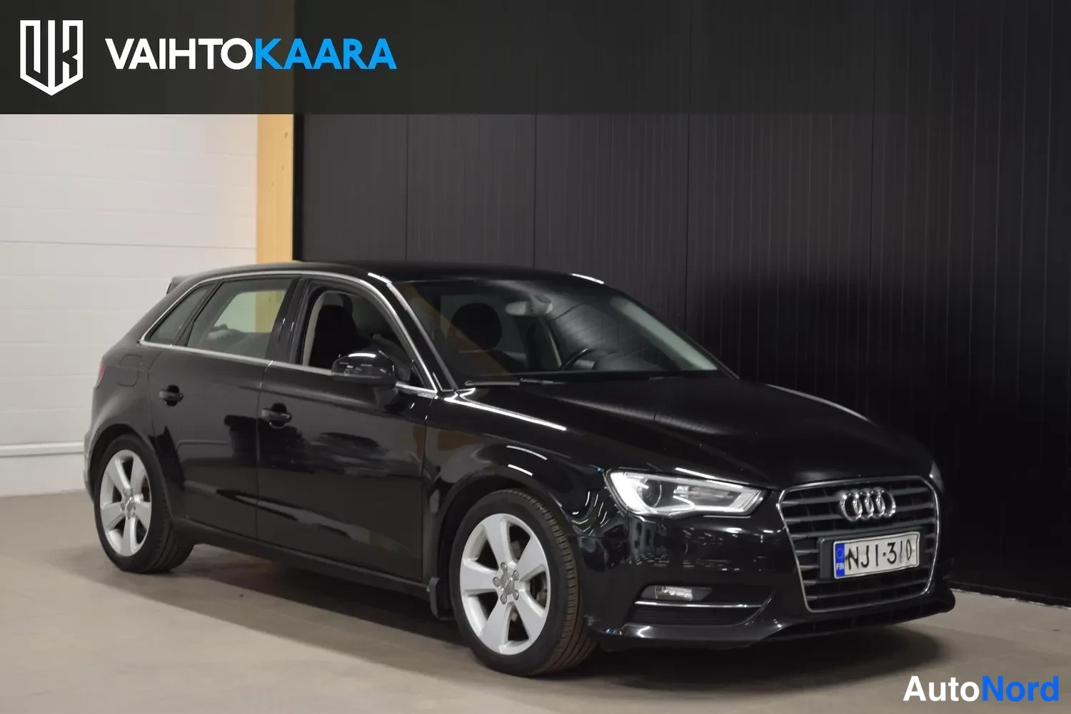 Etuviisto, nokka oikealle: Musta Audi henkilöauto kolmeneljänneskeulaotsakulmasta oikealta, rekisterikilpi.