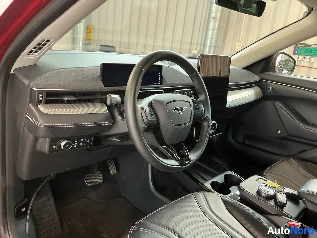 Muu: Mustang Mach-E:n kuljettajan puolen sisätilat: ohjauspyörä Mustang-logolla, pystyyn asennettu suuri keskiryhmän kosketusnäyttö, digitaalinen mittarinäyttö ja mu