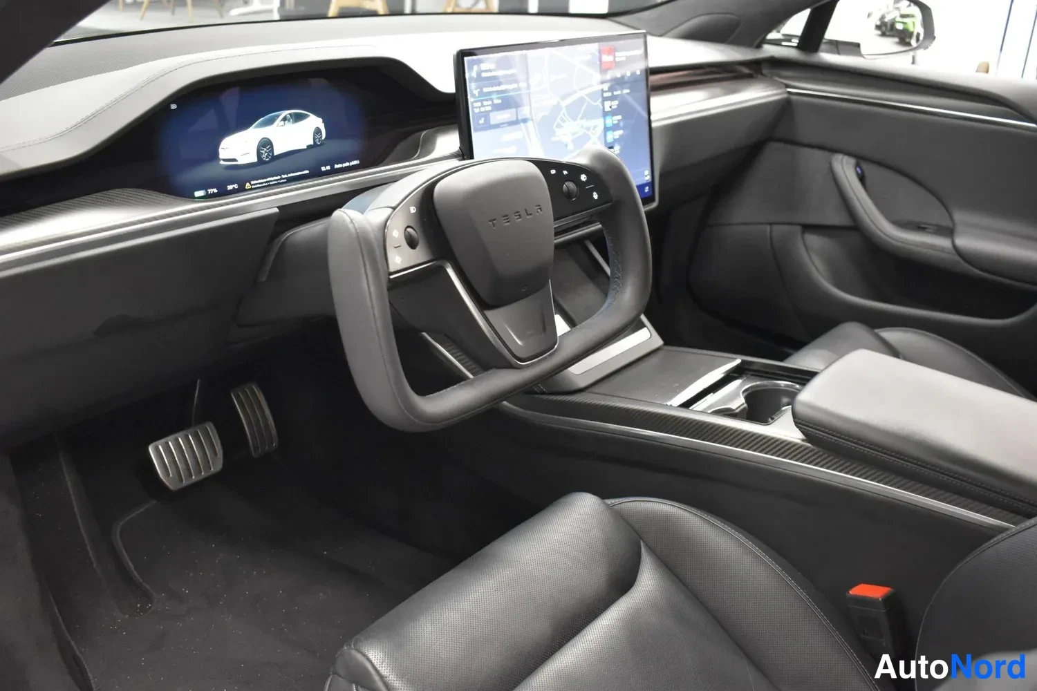 Edestä: Sisäkuvaa Tesla Model S -autosta: ohjauspyörä, keskikonsolin suuri kosketusnäyttö ja mittarinäyttö näkyvät.
