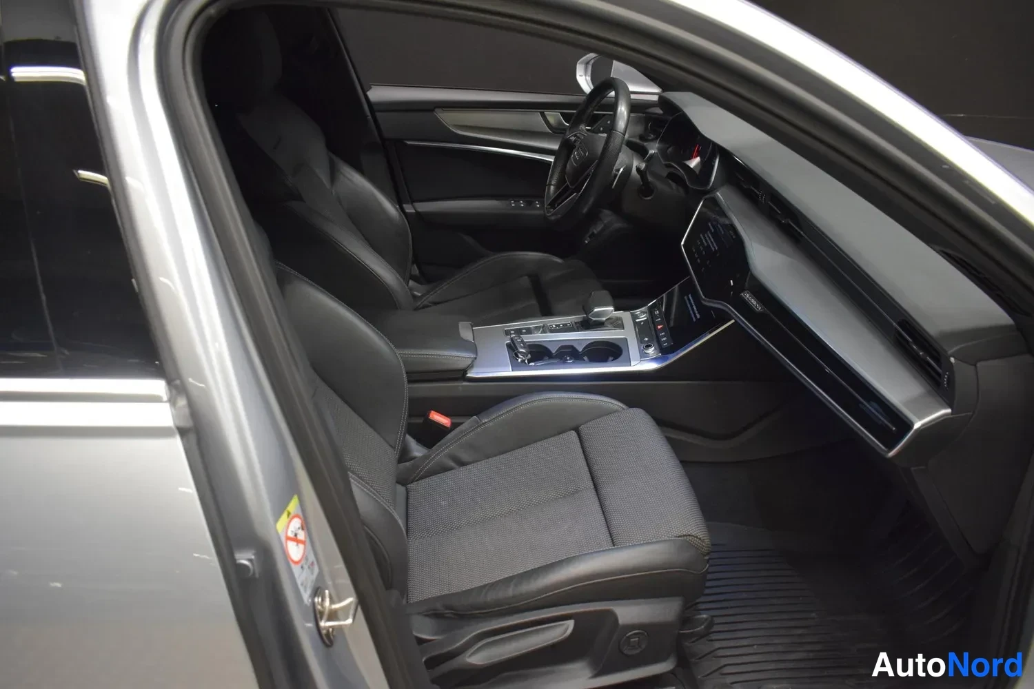 Muu: Audi A6:n ohjaamo kuvattuna avatun takaoven kautta: etuistuimet, keski­konsoli ja dashboard näkyvät.