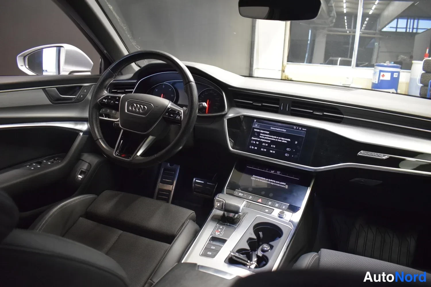 Muu: Audi A6:n ohjaamo kuljettajan puolelta: AUDI-ohjauspyörä, mittarit ja kaksi kosketusnäyttöä, joissa suomenkielisiä valikkoja.