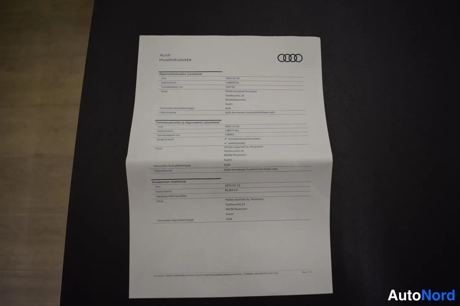 Muu: Audi-huoltotuloste pöydällä, jossa huolto- ja katsastustiedot vuosilta 2023–2024.