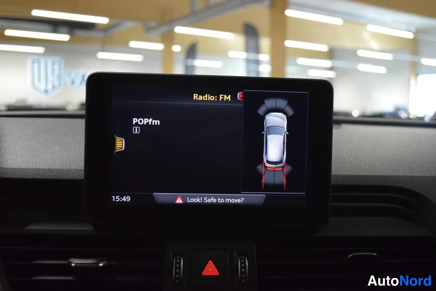 Muu: Istumaveden peili: Auton infotainment-näyttö näyttää radiovalikon (Radio: FM, POPfm), kellonajan 15:49 ja pysäköintitutkan grafiikan alusta.