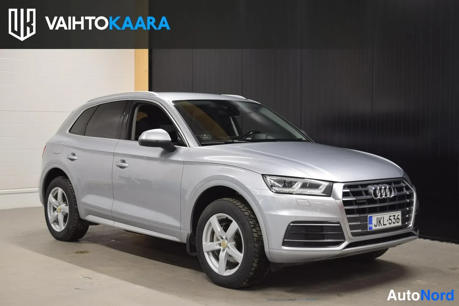 Etuviisto, nokka oikealle: Audi Q5 -maasturin etunurkkikuva oikealta: hopeakorinen auto, etusäleikö ja rekisteri näkyvissä, kevytmetallivanteet.