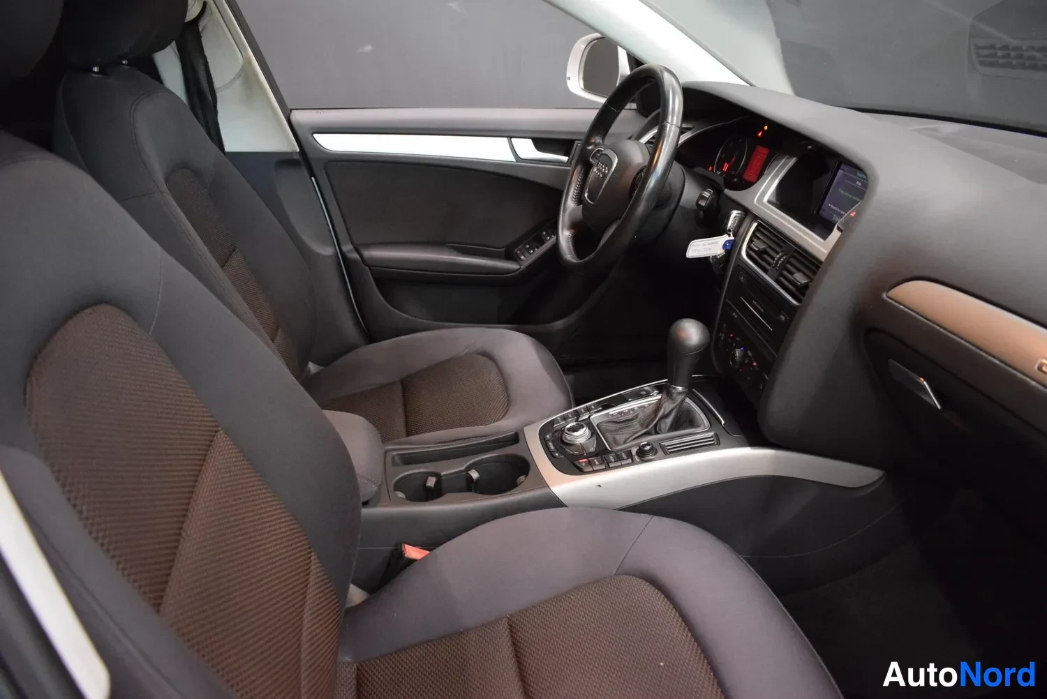 Muu: Audi A4:n sisätilat etuistuimilta kuvattuna: kaksi tummaa kangasistuinta, ohjauspyörä ja vaihdekepki keskikonsolissa.