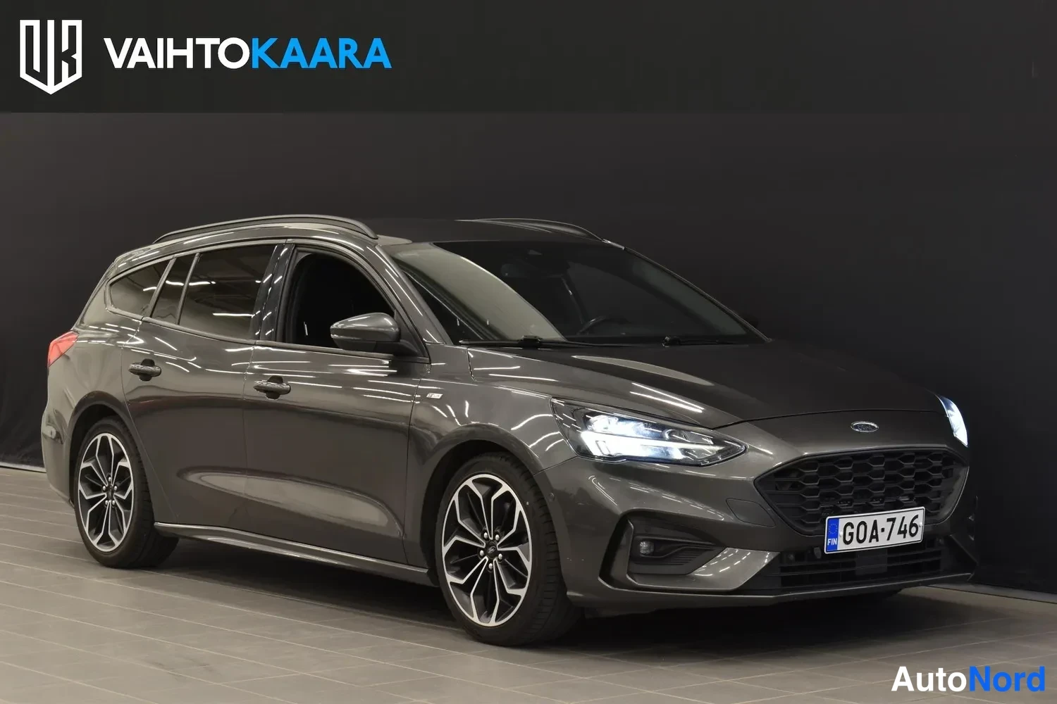 Etuviisto, nokka oikealle: Tummanharmaa Ford Focus -farmari etuviistossa oikeaan kulmassa, rekisterikilpi.