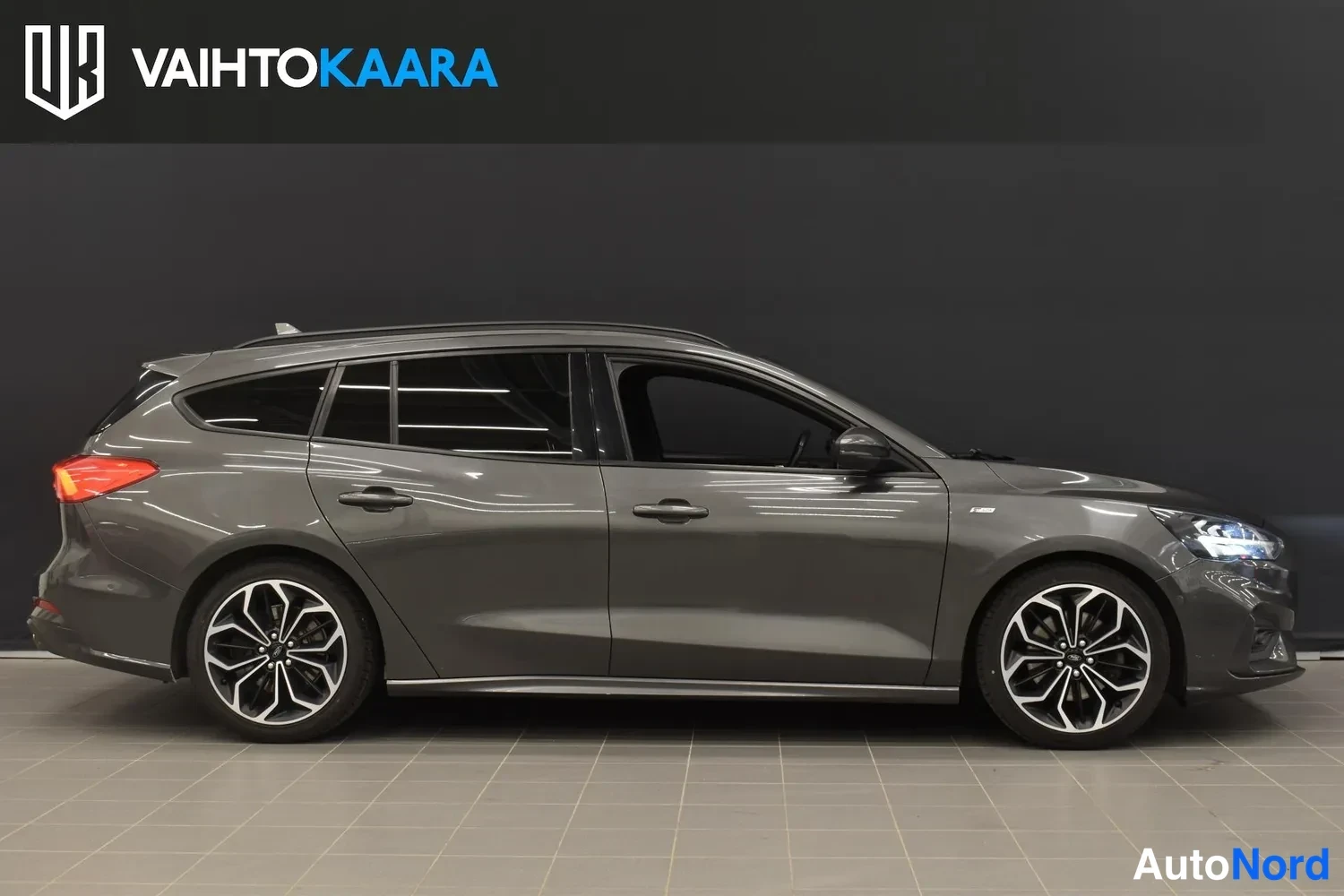 Etuviisto, nokka oikealle: Tummanharmaan Ford Focus -farmarin sivukuva oikealta puolelta studiossamaisessa valaistuksessa.