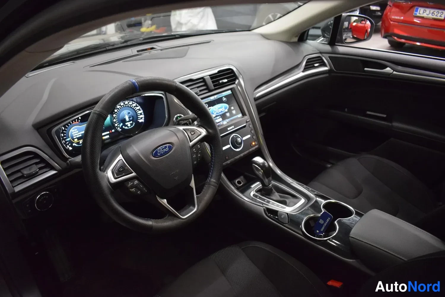 Sivulta: Ohjaamo vasemmalta etualalta: ratissa Ford-logo, mittaristo ja kosketusnäyttö keskikonsolissa, automaattivaihteen valitsin ja kuppitelineet näkyvät.