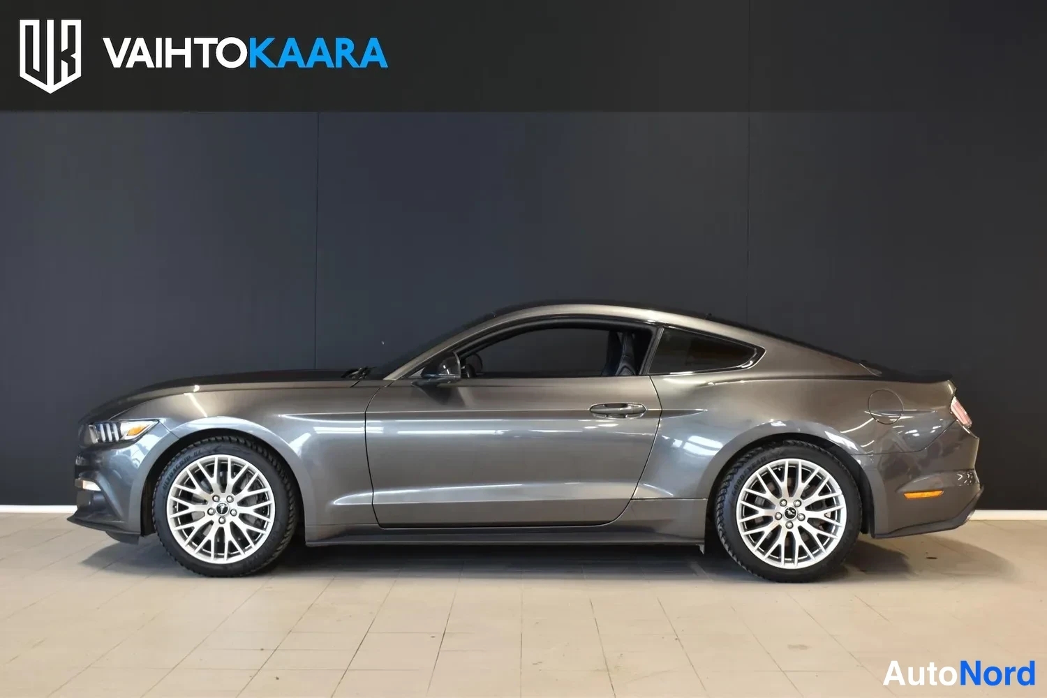 Etuviisto, nokka vasemmalle: Ford Mustang sivukuva, tummanharmaa coupé hallitilassa.