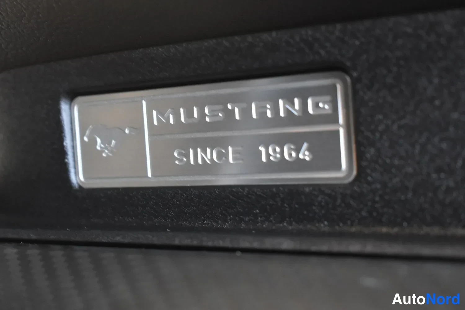 Yksityiskohta: Lähikuva Ford Mustang -kilvestä, jossa lukee MUSTANG SINCE 1964.