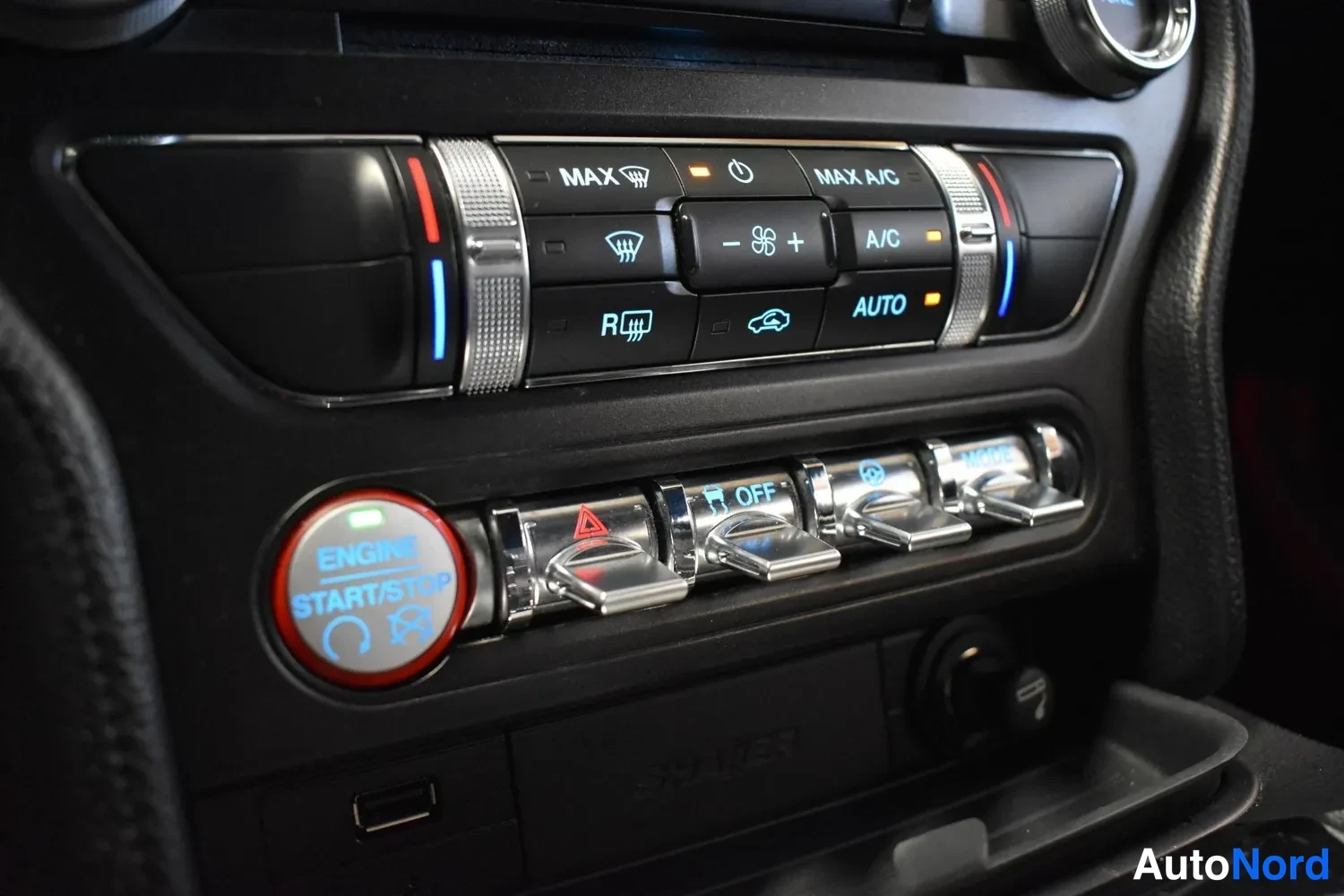 Muu: Ford Mustangin kojelaudan ilmastointipaneeli MAX-, A/C- ja AUTO-näppäimillä sekä ENGINE START/STOP-painike ja toggle-kytkimiä.