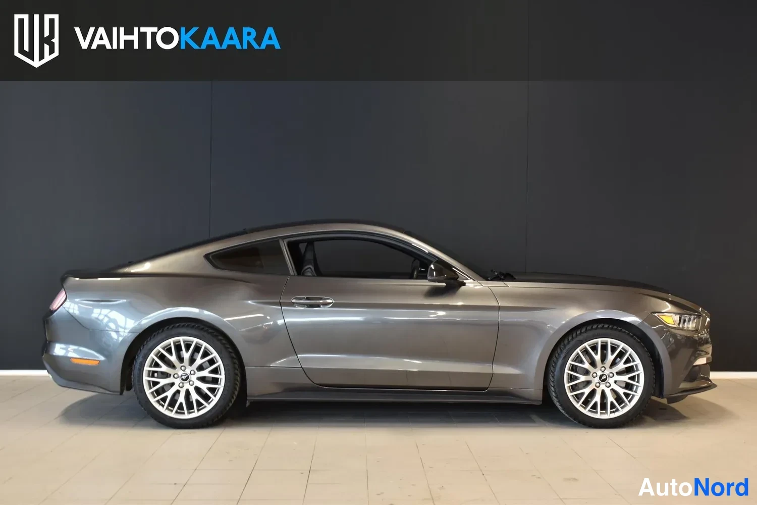 Sivulta: Ford Mustang -porrasperä sivulta tummanharmaana, hopeavanteiset pyörät ja mustat lasit mustaa taustaa vasten.
