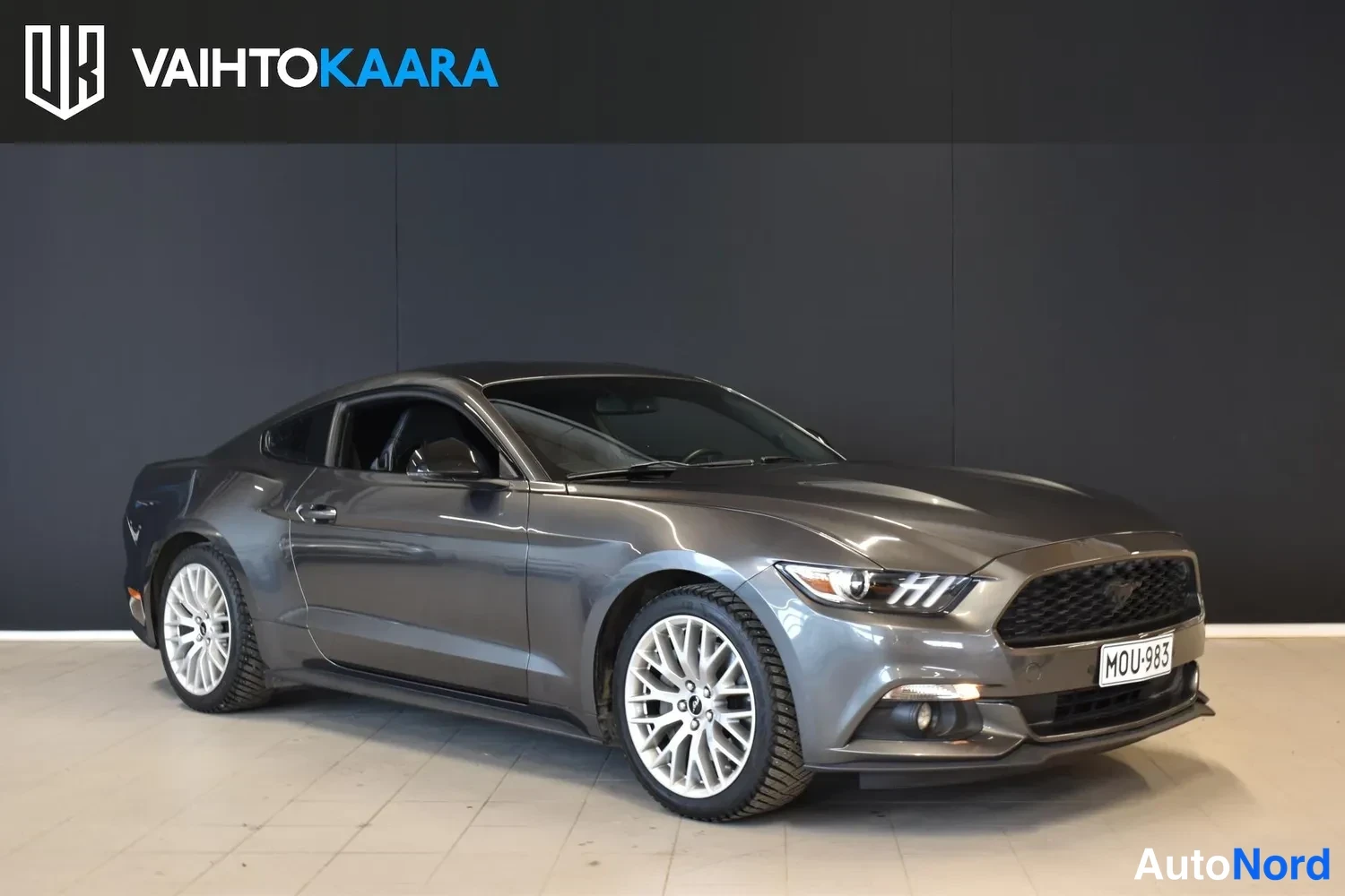 Etuviisto, nokka oikealle: Ford Mustang etuviistöstä oikealta, tummanharmaa kori, keulassa koneikkasuojus ja rekisteri.