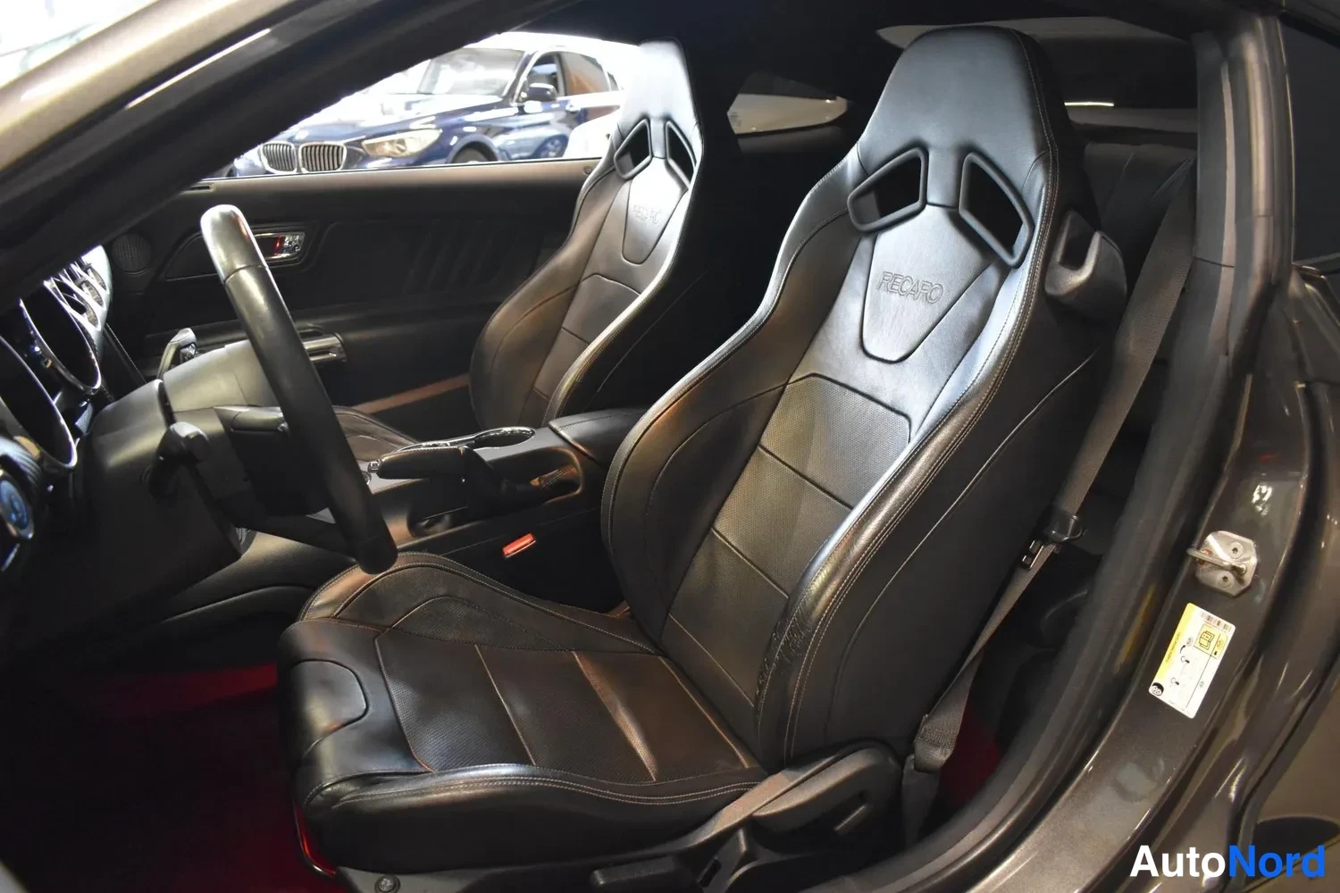 Muu: Mustan nahkainen Recaro-urheiluistuin Ford Mustangin etuistuinriviltä, taustalla toinen etuistuin ja ikkunasta autotallin katselmus.