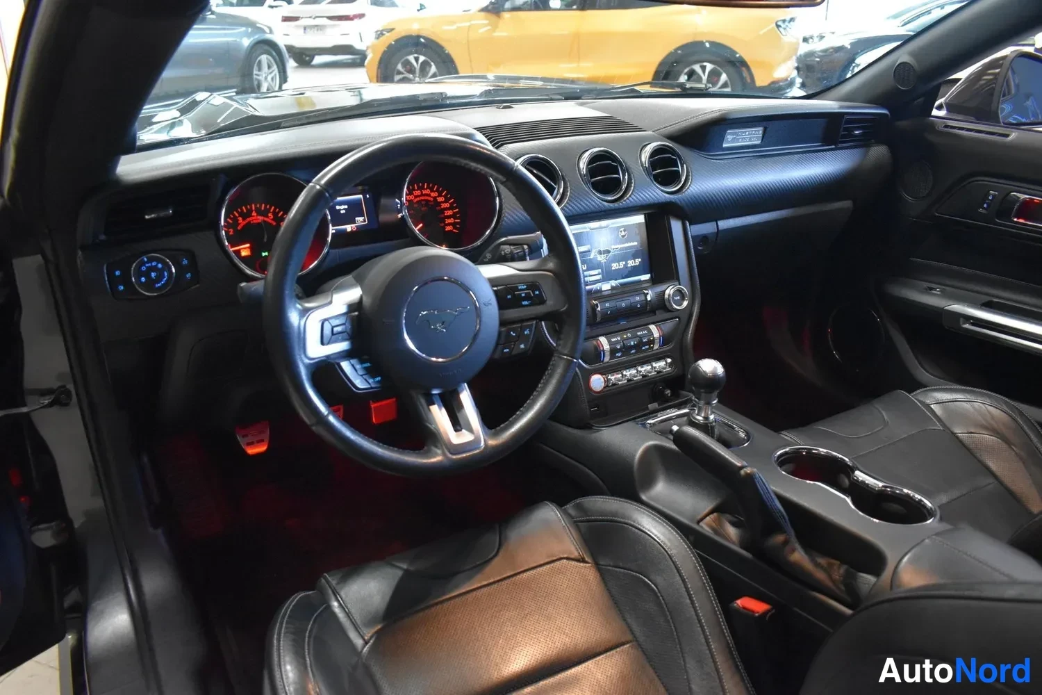 Muu: Ford Mustangin ohjaamosta näkyy Ford-merkkinen ohjauspyörä, analogiset mittarit, kosketusnäyttö ja vaihtokeppiklabi manuaalivaihteistoon; punainen väliestyöpöyd