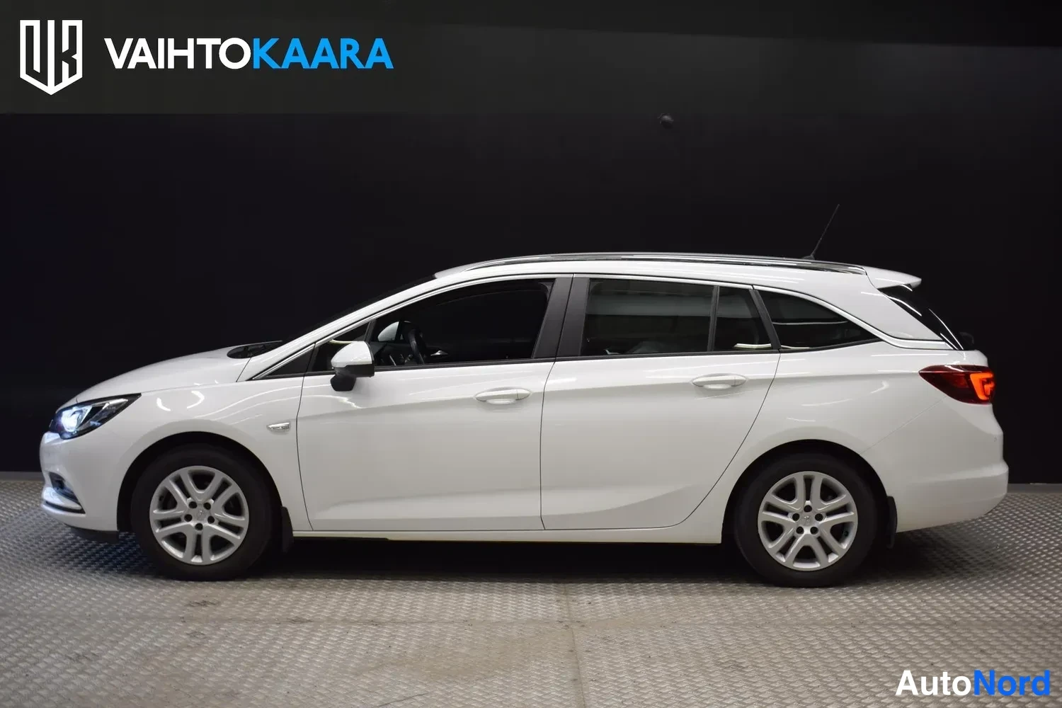 Etuviisto, nokka vasemmalle: Opel Astra Sports Tourer -farmari sivulta vasemmalta, valkoinen kori ja moniosaiset alumiinivanteet.