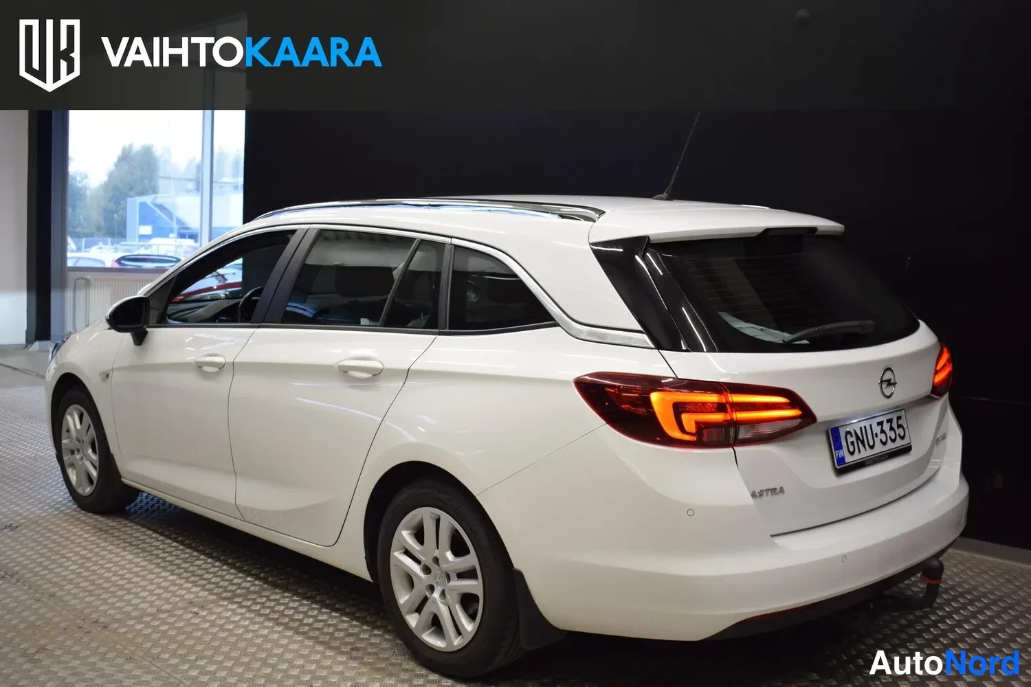 Takaviisto: Opel Astra Sports Tourer -farmari takaa oikealta, valkoinen koripelti ja tummat takavalot. Rekisteritunnus.