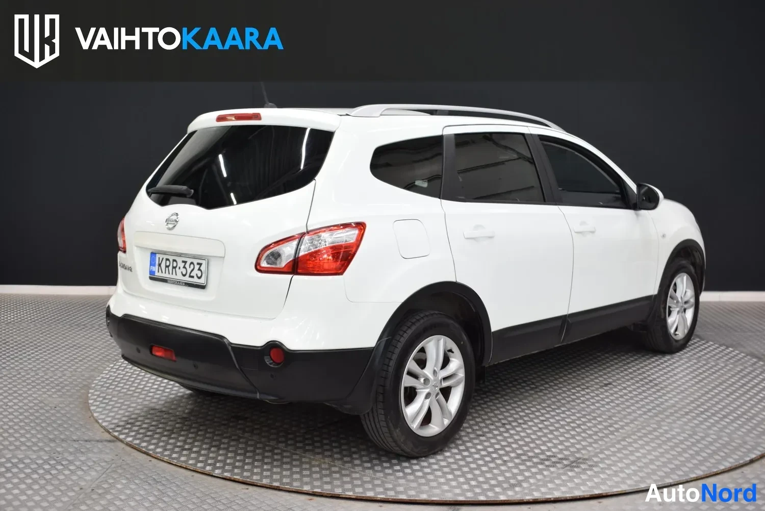 Takaviisto: Valkoisen Nissan Qashqai+2:n takakulmakuva vasemmalta, takapanssari ja kylki näkyvät studioissa.