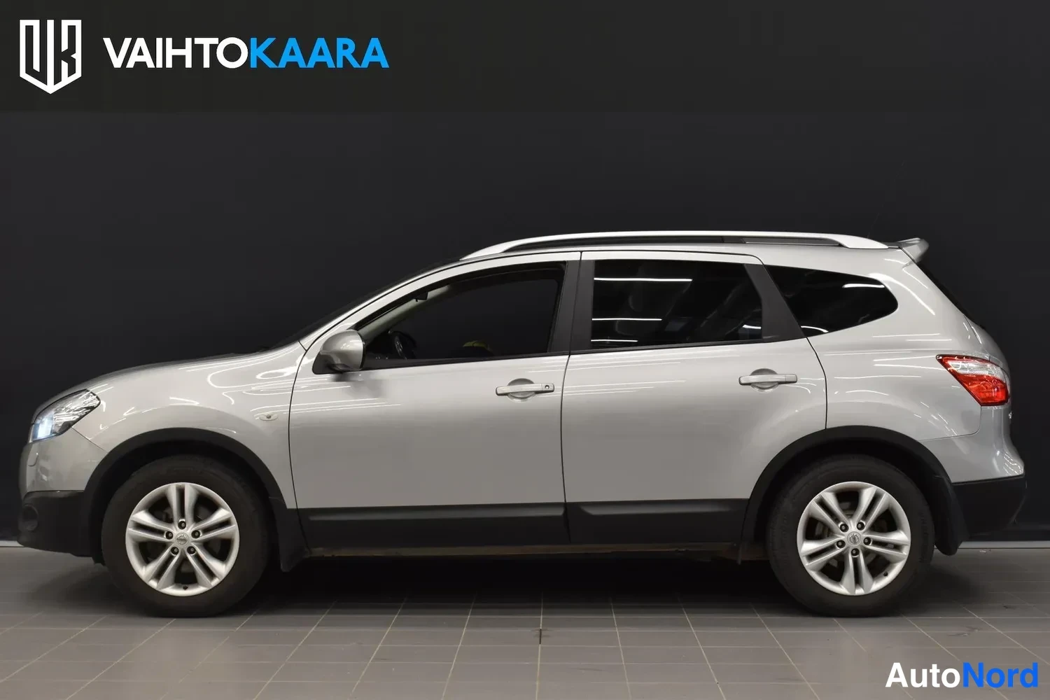Sivulta: Nissan Qashqai+2 -henkilöauton sivuprofiili, hopeinen, kuvattuna sisätilassa.