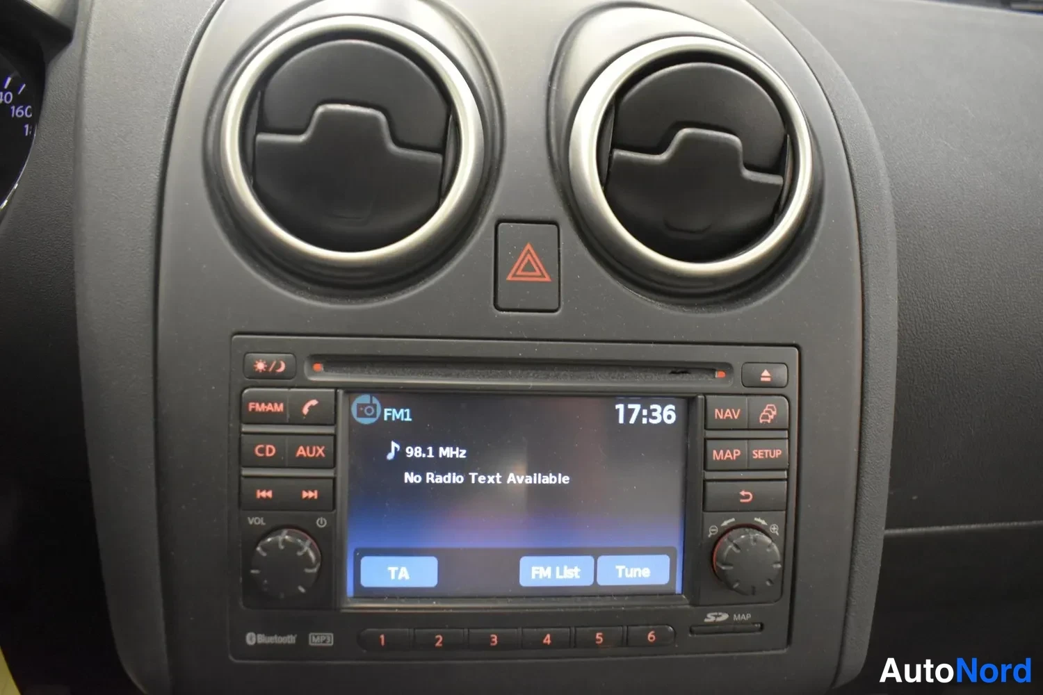 Yksityiskohta: Keskikonsolin radio ja kaksi pyöreää ilmastointisuutinta; näytöllä FM1, 98.1 MHz, aikana 17:36; NAV-, MAP-, SETUP- ja CD/AUX-painikkeet.