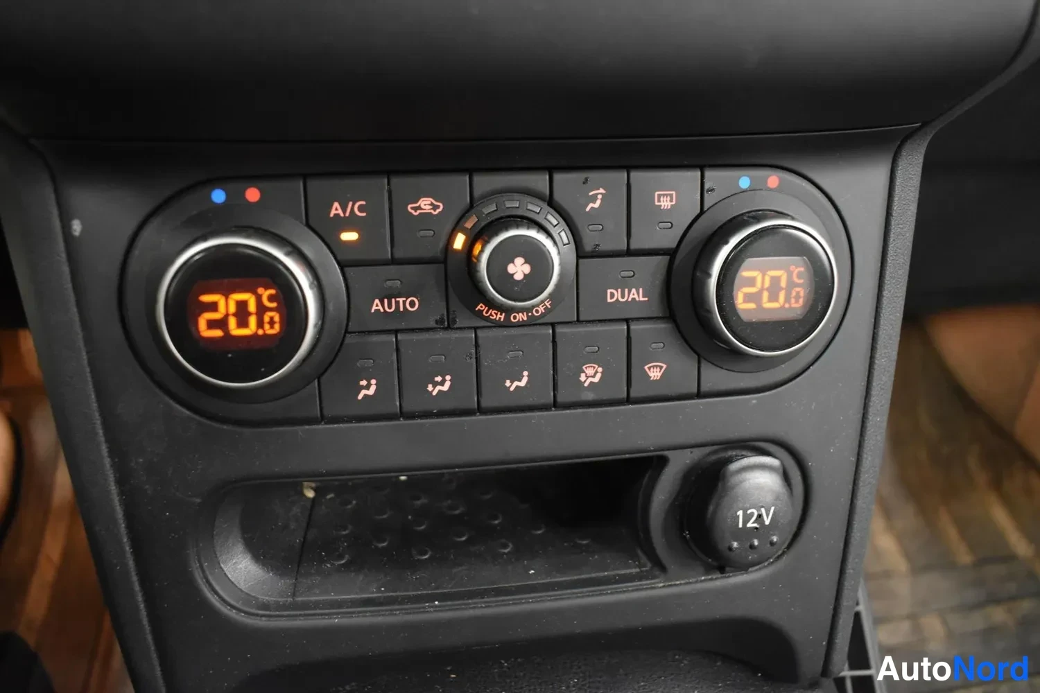 Muu: Autoa kirjaimellisesti: keskikonsolin ilmastointipaneeli, jossa on kaksi digitaalista lämpötilanäyttöä (20 °C), A/C-, AUTO- ja DUAL-merkit sekä 12 V -pistorasia