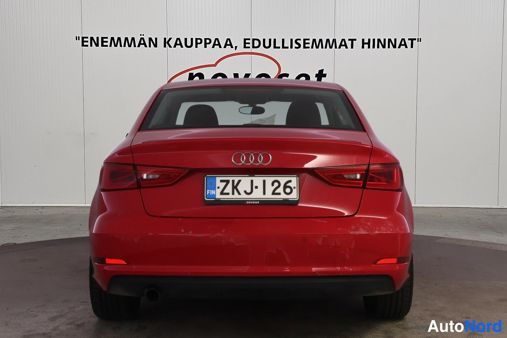 Takaa: Punaisen sedanin suora takaostakuva, Audi-merkki, punaiset takavalot, rekisterikilpi.