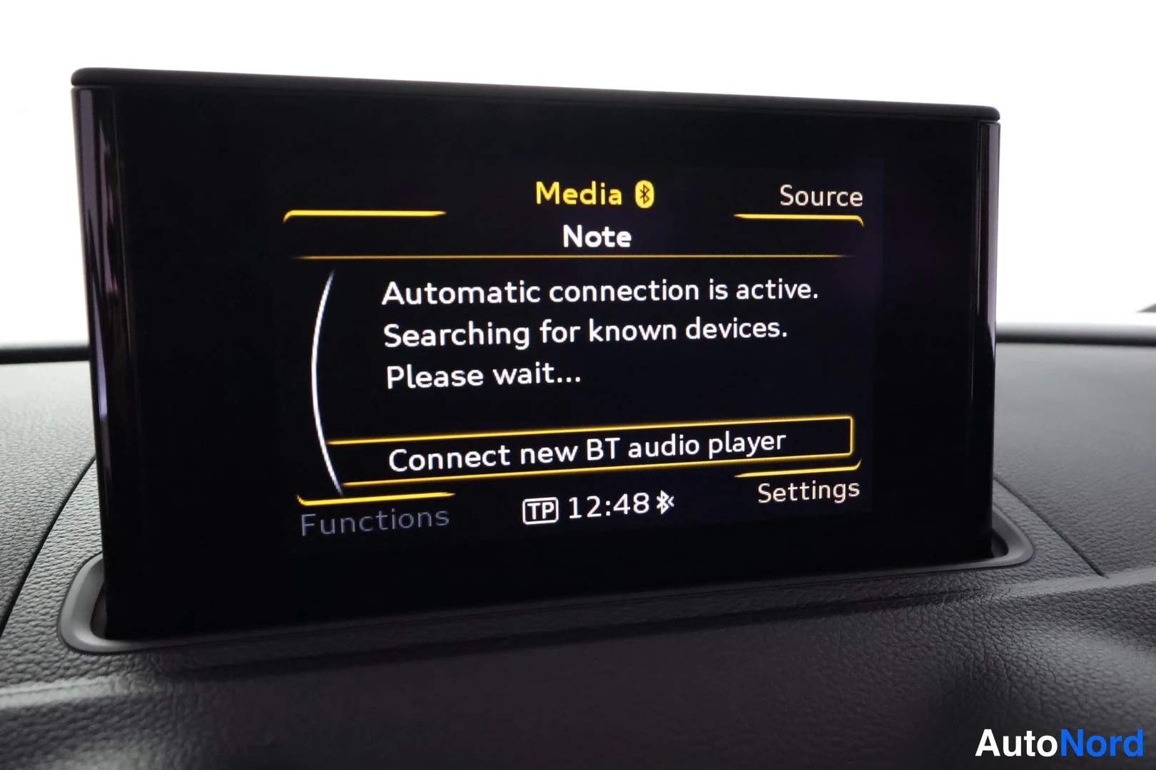 Yksityiskohta: Kojelaudan infotainment-näyttö, jossa Bluetooth-median hakuviesti ja kello 12:48.