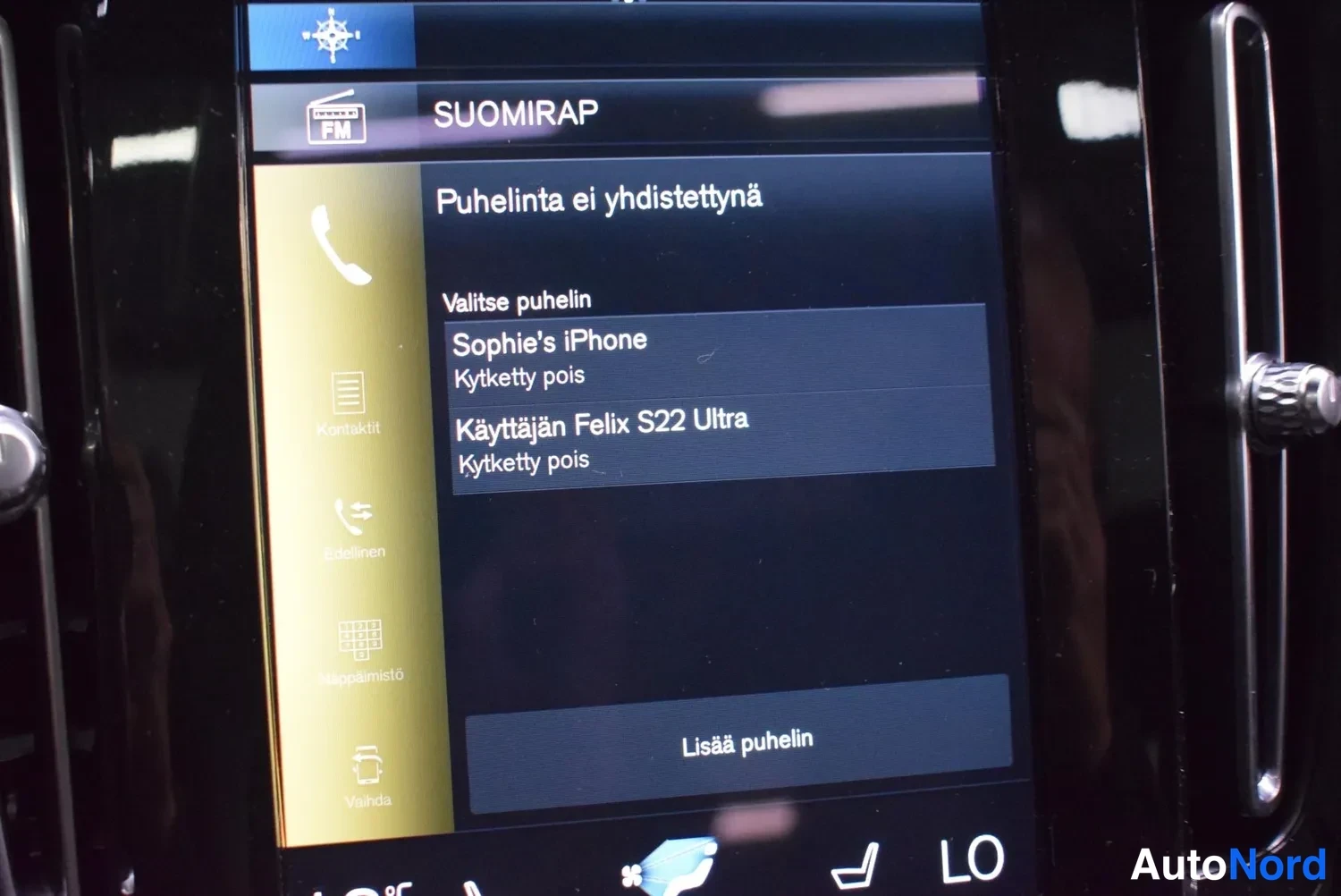 Yksityiskohta: Infotainment-näytön puhelinvalikko: 'Puhelinta ei yhdistettyä', luettelossa 'Sophie's iPhone' ja 'Käyttäjän Felix S22 Ultra', molemmat 'Kytketty pois', painike