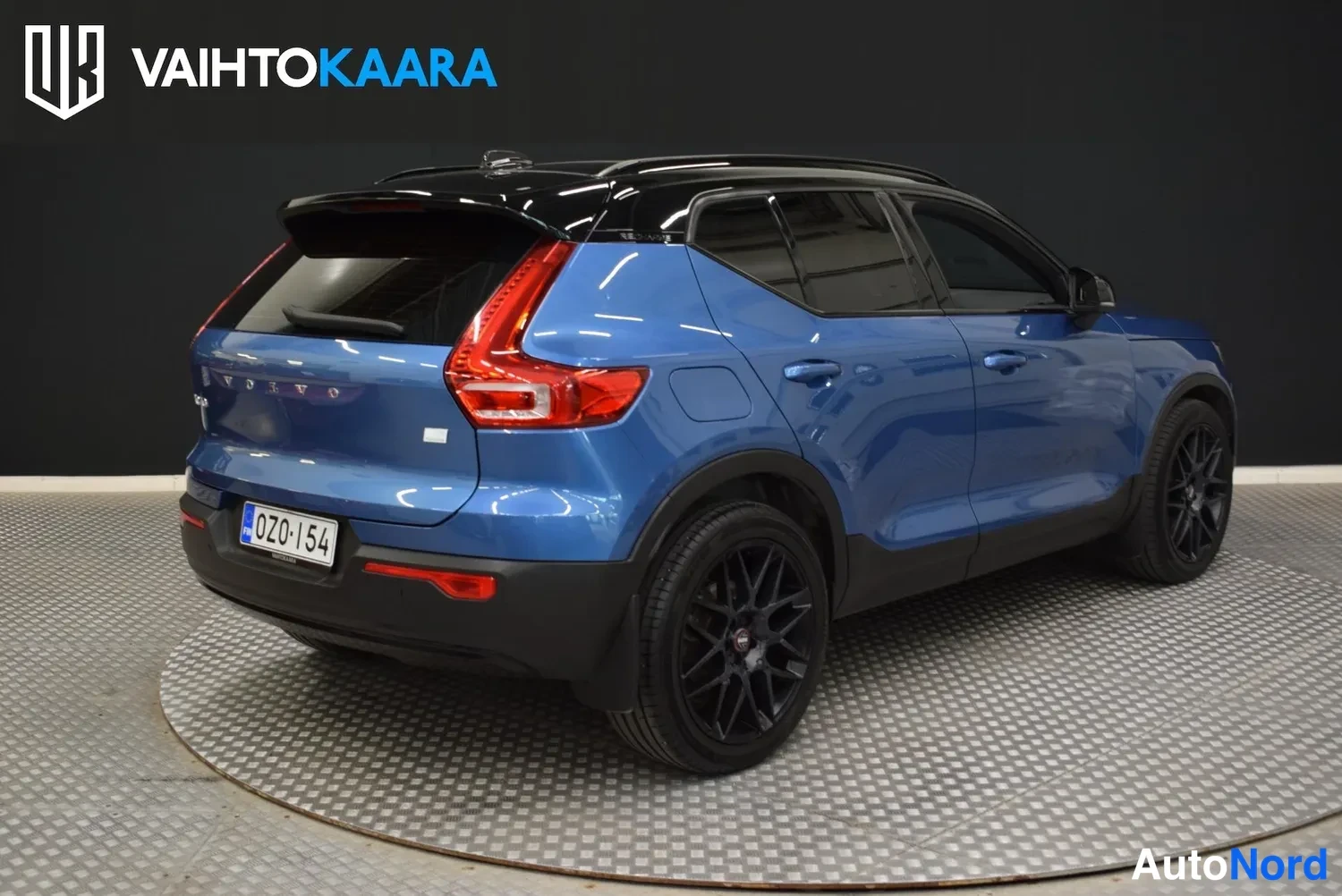 Takaviisto: Sininen Volvo XC40 takaviistosta toisesta kulmasta, punaiset takavalot, musta katto ja kiiltävät mustat vanteet, rekisteritunnus.
