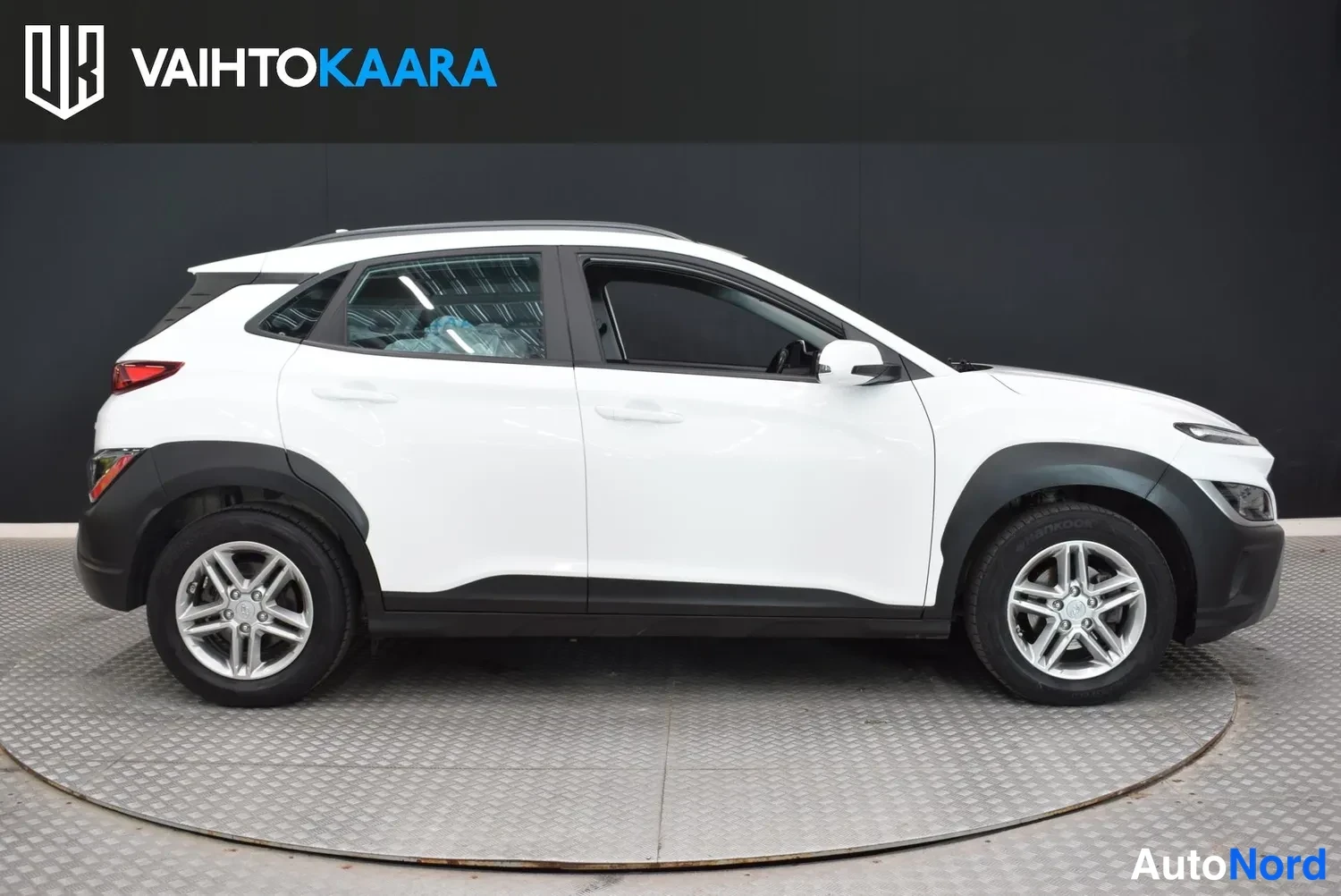 Sivulta: Hyundai Kona -auto sivusta kuvattuna, valkoinen korimalli tummassa studiossa.