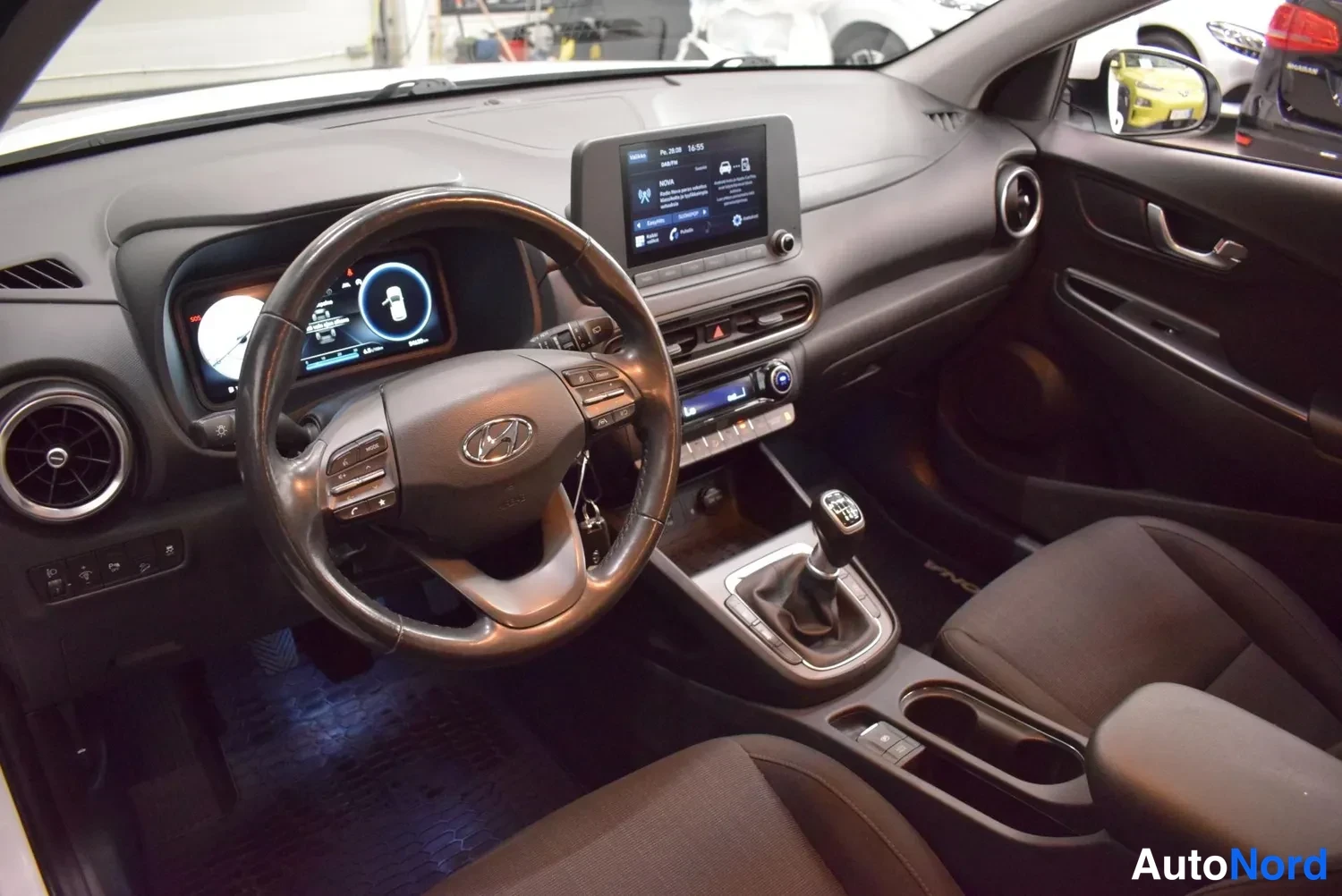 Muu: Hyundai Kona:n ohjaamo etupäästä: ratti, kosketusnäyttö ja manuaalivaihteiston vaihdevipu.
