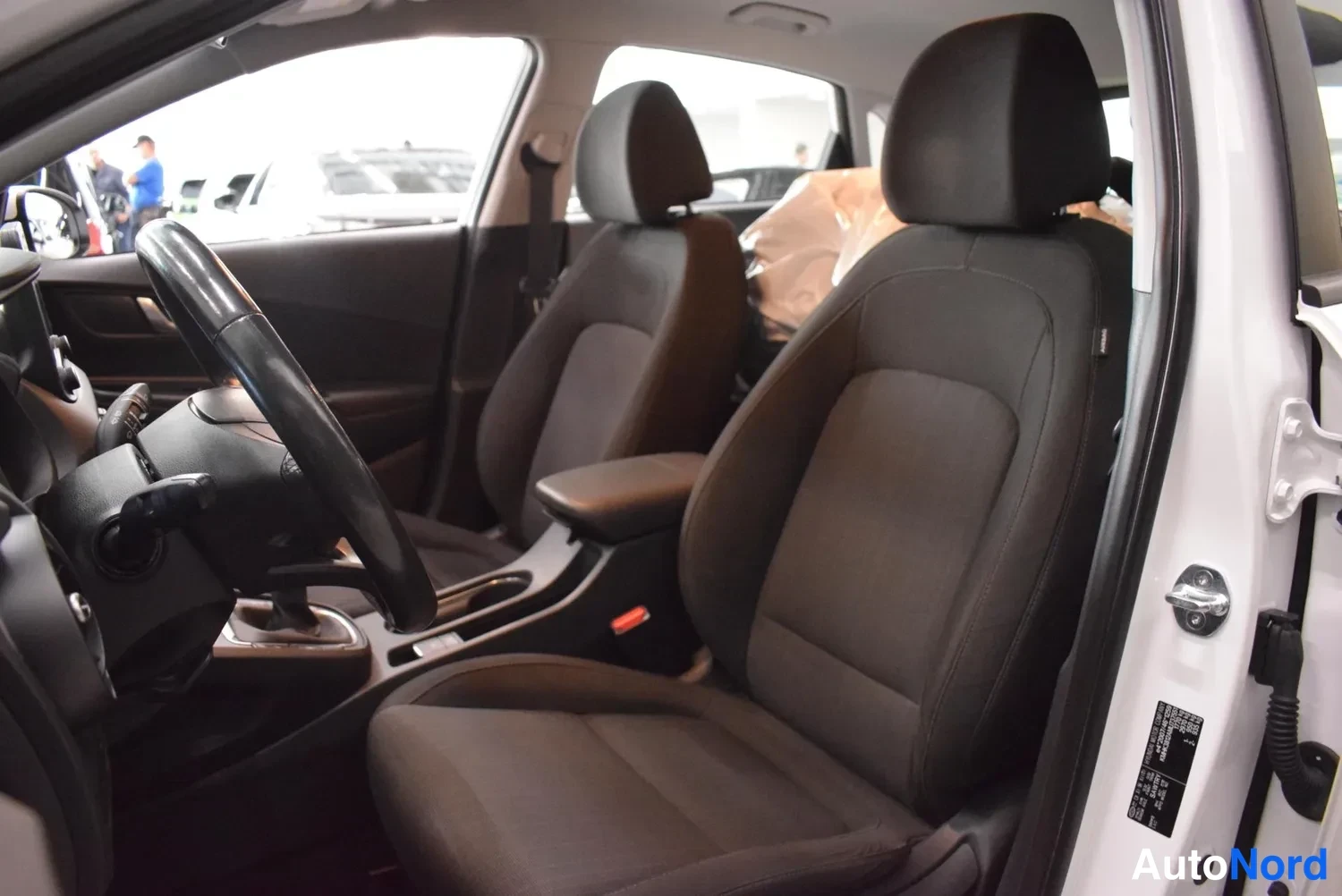 Muu: Avoimen etuoven näkymä Hyundai Konan etusohvaan: tummansävyiset kangasistuimet, ohjauspyörä ja keskikonsoli näkyvät.