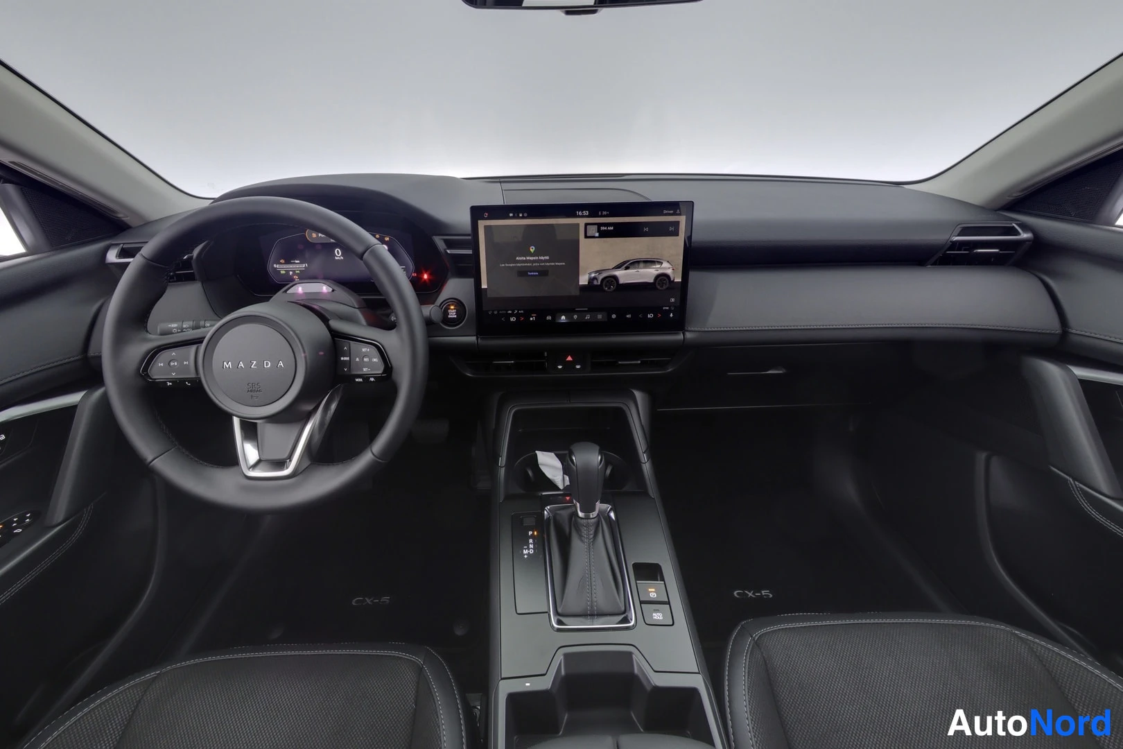 Muu: Ohjaamo kuvattuna takaa: Mazda-ohjauspyörä, digitaalinen mittaristo, keskikonsolin kosketusnäyttö ja automaattivaihteiston valitsin.