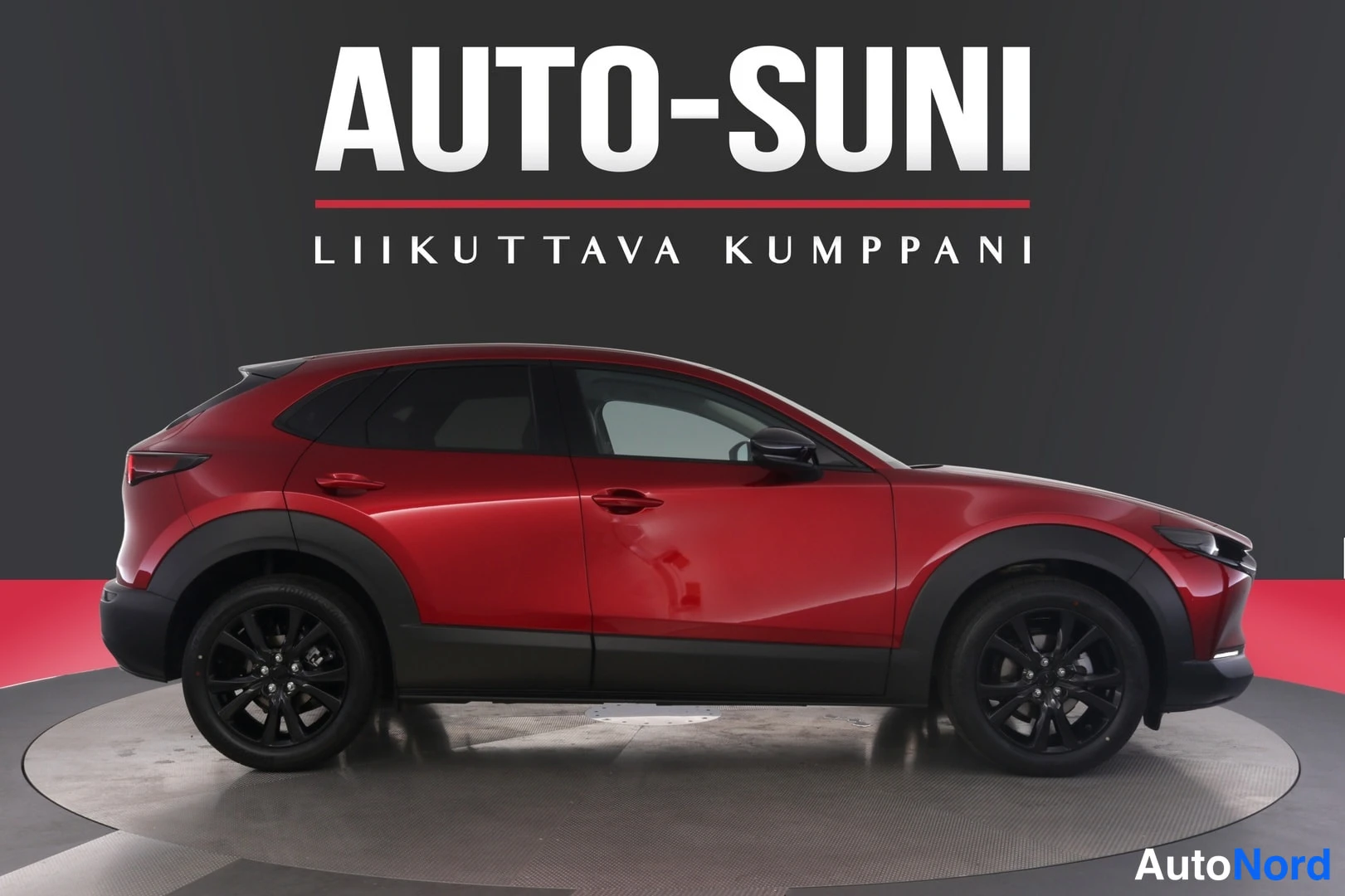 Sivulta: Punainen Mazda CX-30 sivukulmassa oikealta vasemmalle studion pyörivällä alustalla, mustat vanteet.