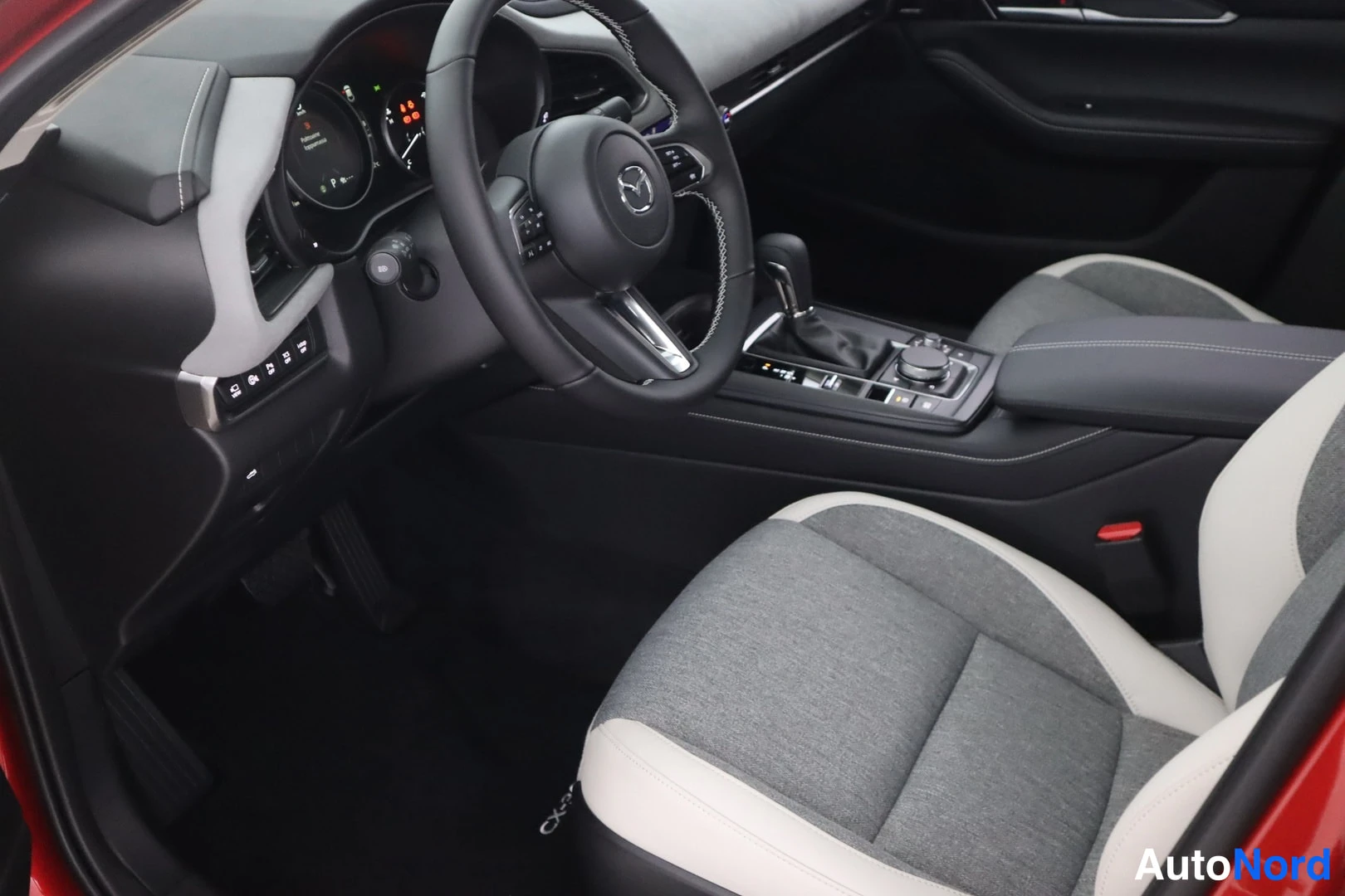 Muu: Ohjaamo vasemmalta: Mazda-ohjauspyörä, automaattivaihteen valitsin ja harmaa-valkoinen kojiaverhoilu.