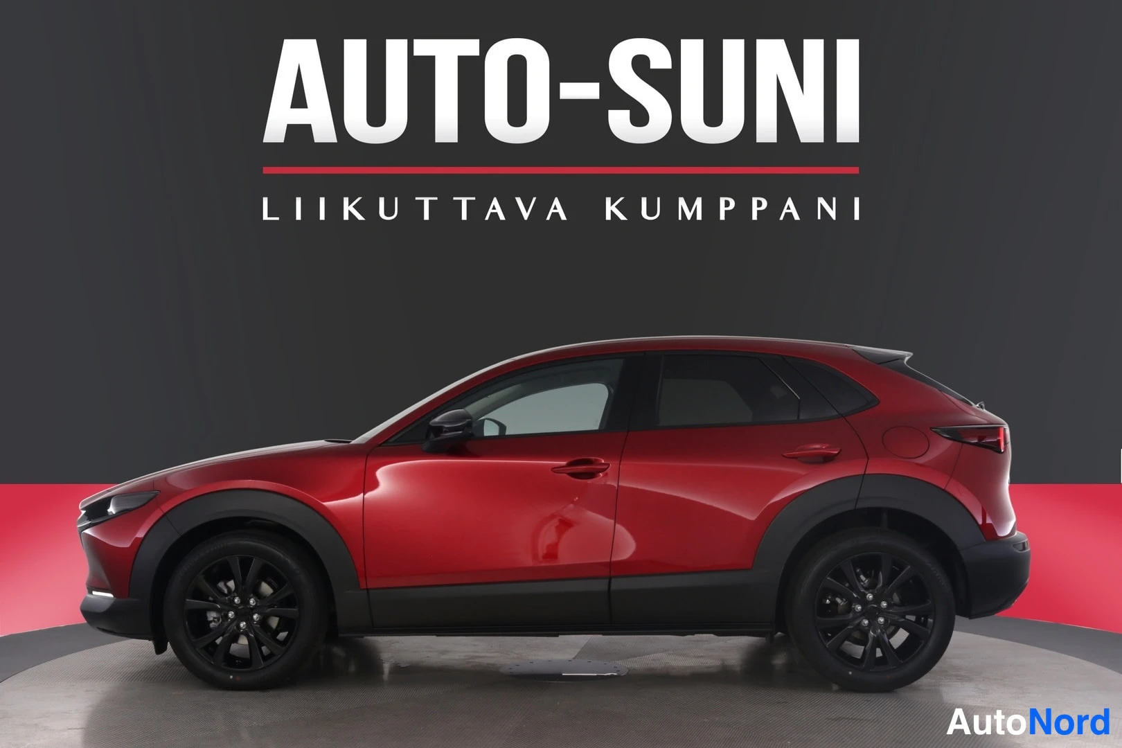 Sivulta: Punaisen Mazda CX-30:n sivuprofiili studiotaustaa vasten, mustat vanteet ja showroom-merkintä kuvassa.
