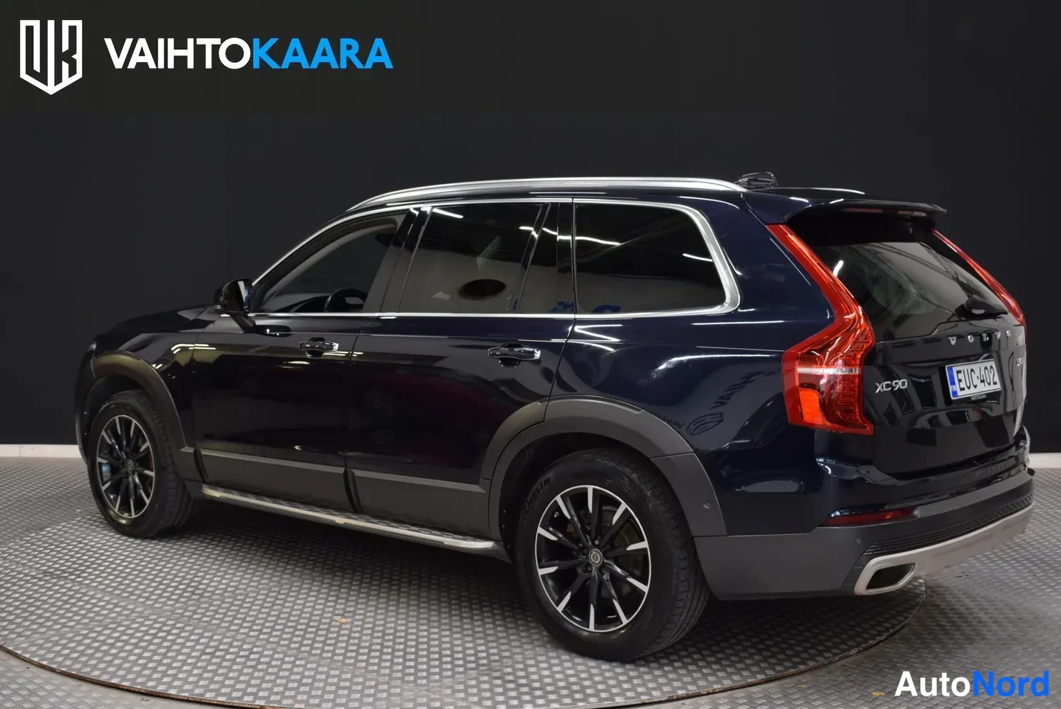 Takaviisto: Tummansininen Volvo XC90 -maasturia kuvattu takaa kolmannesvasemmalta studio Lavassa, takavalot ja rekisterikilpi näkyvissä.