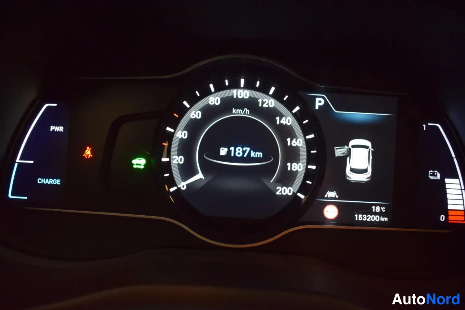 Muu: Sähköauton mittaristo lähikuvassa: nopeusmittari, PWR- ja CHARGE-mittarit, jäämä 187 km, P-vaihteen merkki ja lukema 153200 km.