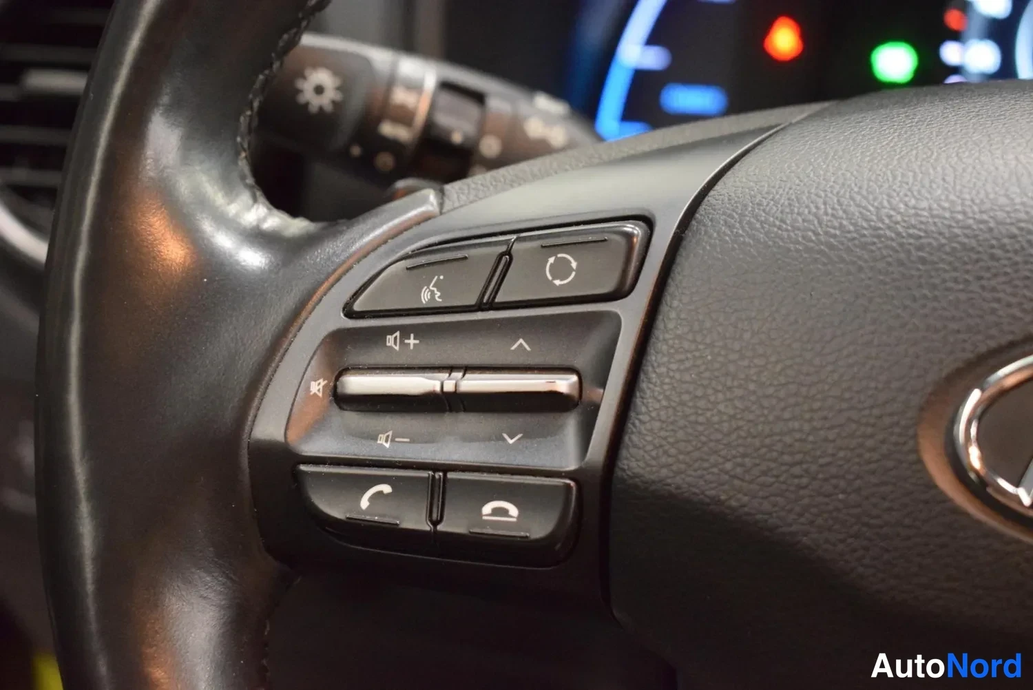 Yksityiskohta: Rattens vänstra knappanel med knappar för telefon, volym och röststyrning samt Hyundai-logotyp på ratten.