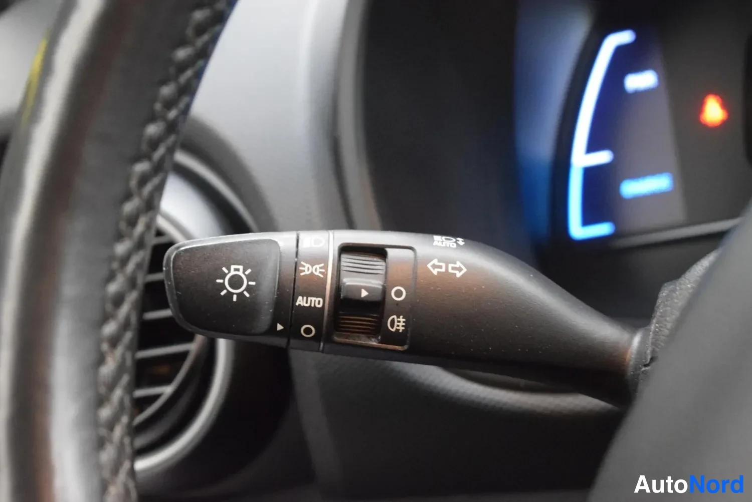 Yksityiskohta: Ljusbrytaren har läget AUTO och symboler för ljus och dimljus, bakom syns instrumentpanelen med blå skärm.