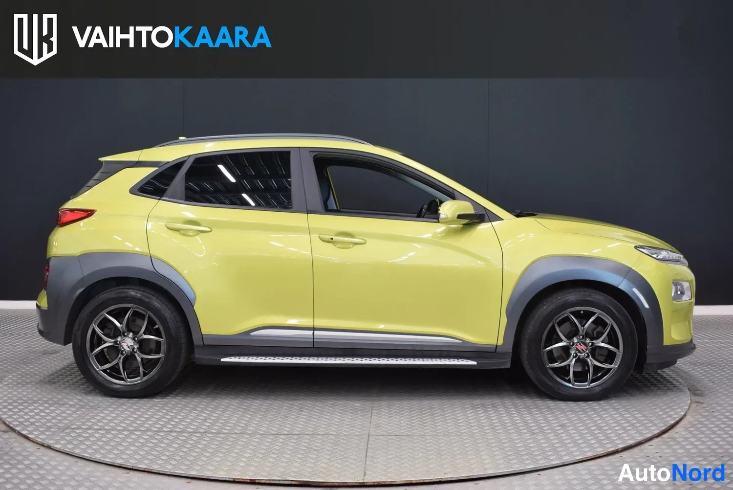 Etuviisto, nokka oikealle: Hyundai Kona Electric sivulta etukulmasta, keltainen korimalli, mustat kolmipaikkaeväiset kevytmetallivanteet ja sivulatuskella kromilista.