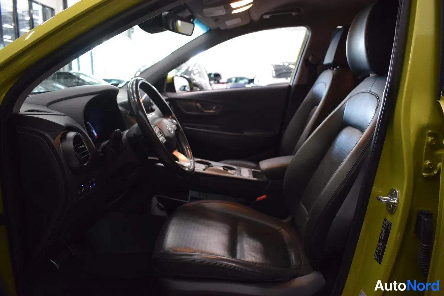 Muu: Hyundai Kona Electricin etumatkustamon sisusta kuljettajan ovi avattuna, tummat istuimet ja ohjaustanko.