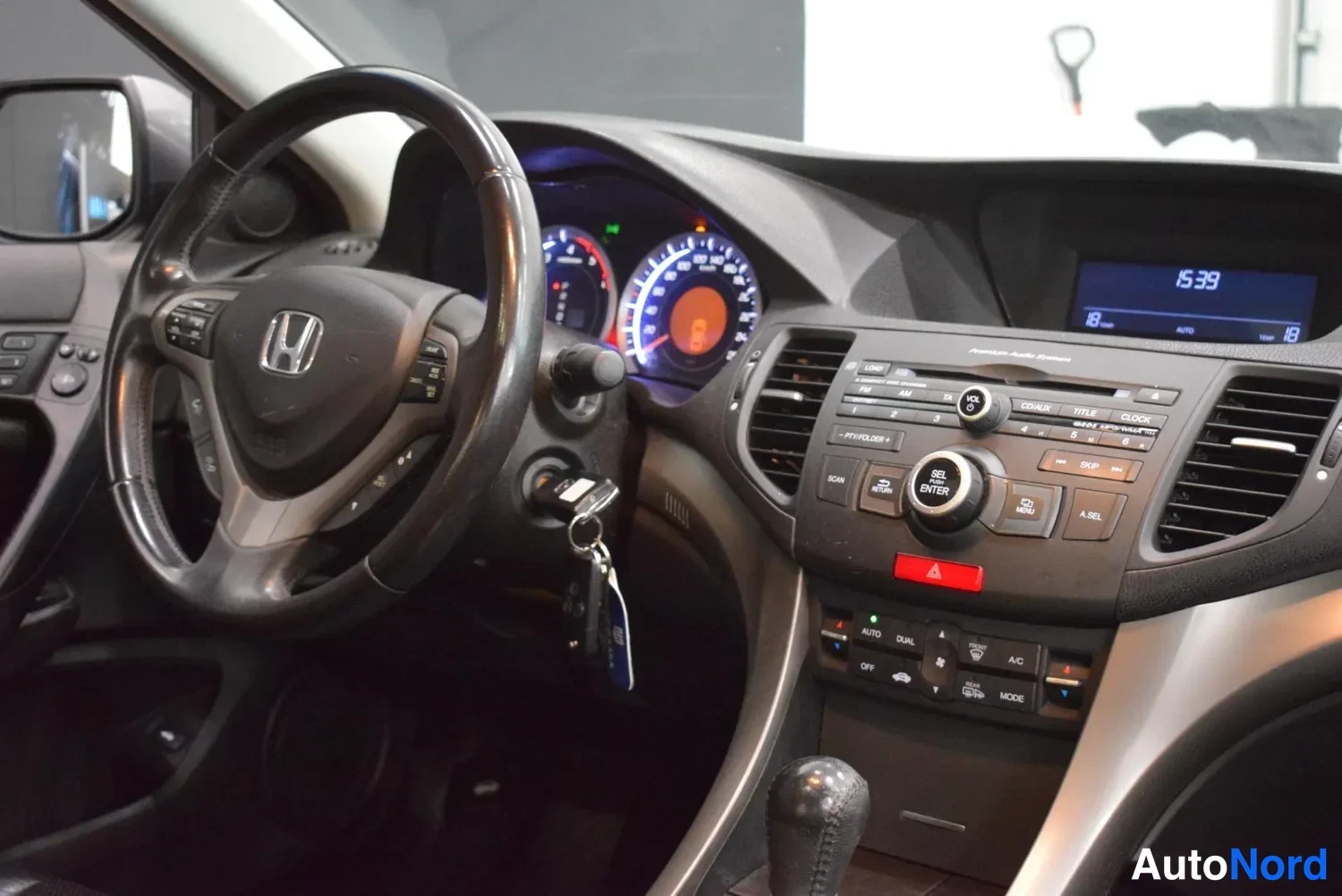 Muu: Kuljettajan näkymä: Honda-ohjauspyörä, mittaristo valaistuna, radio/CD-laite ja avain virtalukossa.