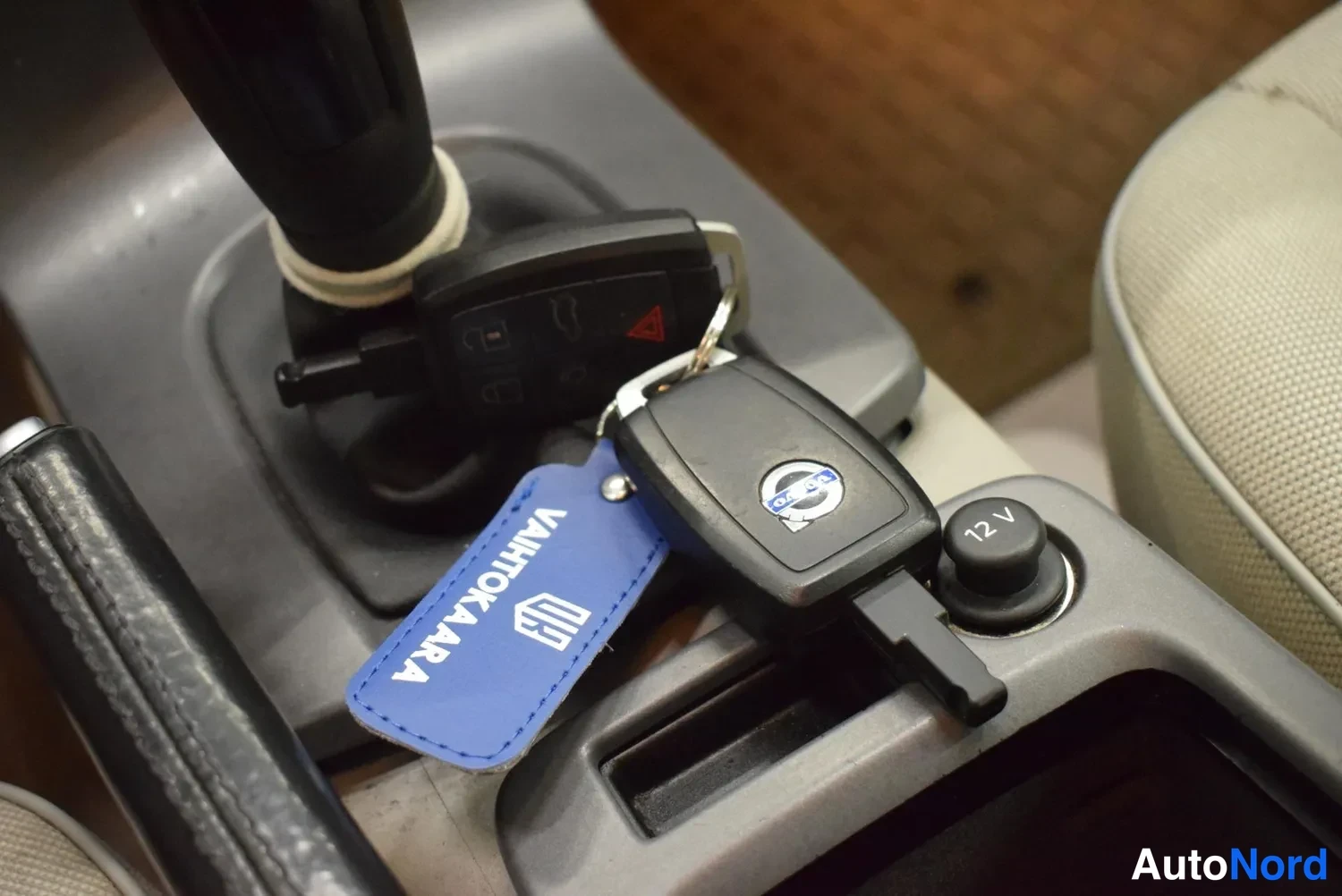 Muu: Kaksi auton avainkaukanaohjainta vaihtokepin vieressä; toisessa Volvo-logo, sininen avainnauha jossa teksti VAHTOKARA.