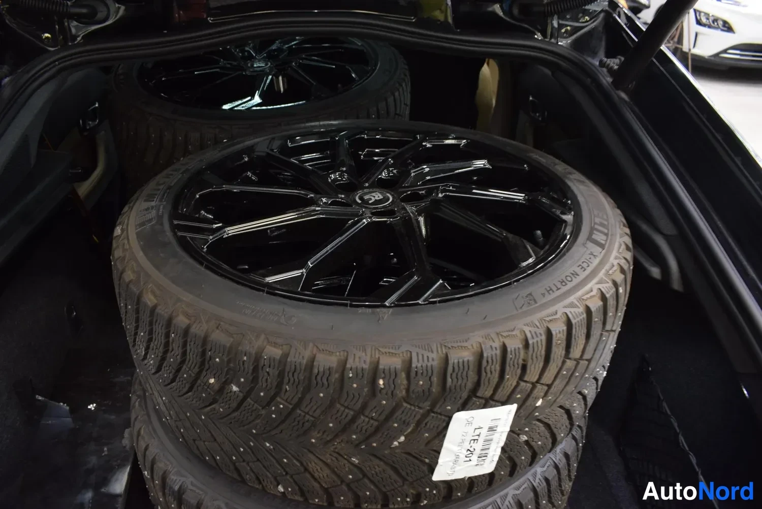 Yksityiskohta: Avatun tavaratilan sisäkuva: pino talvirenkaita kiiltävillä mustilla vanteilla, renkaiden kyljissä Michelin X-Ice North -teksti ja etiketissä LTE 241.