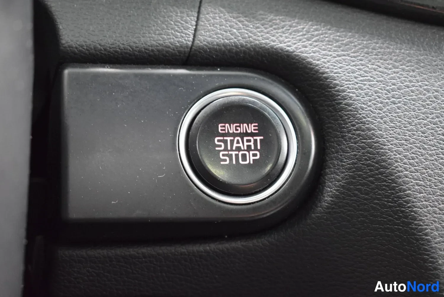 Yksityiskohta: Avaimeton käynnistysnappi lähikuvassa, teksti 'ENGINE START STOP', mustaa nahkapintaista kojelautaa ympärillä.