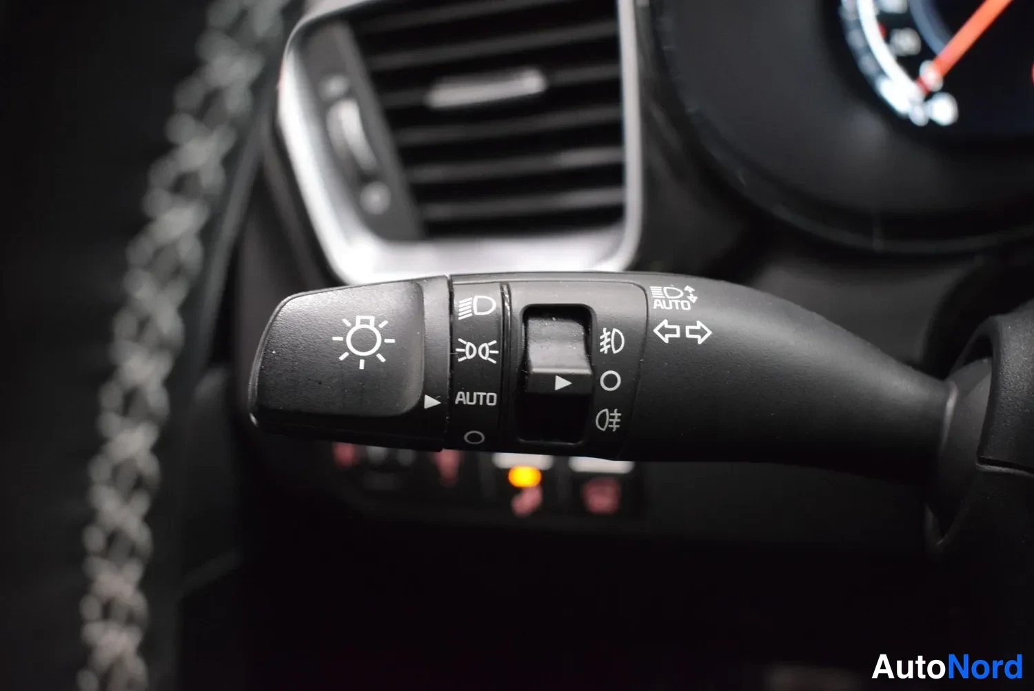 Yksityiskohta: Valokytkimen vipu lähikuvassa AUTO-asennossa; taustalla ilmastointiluukku ja osittain näkyvä mittaristo.
