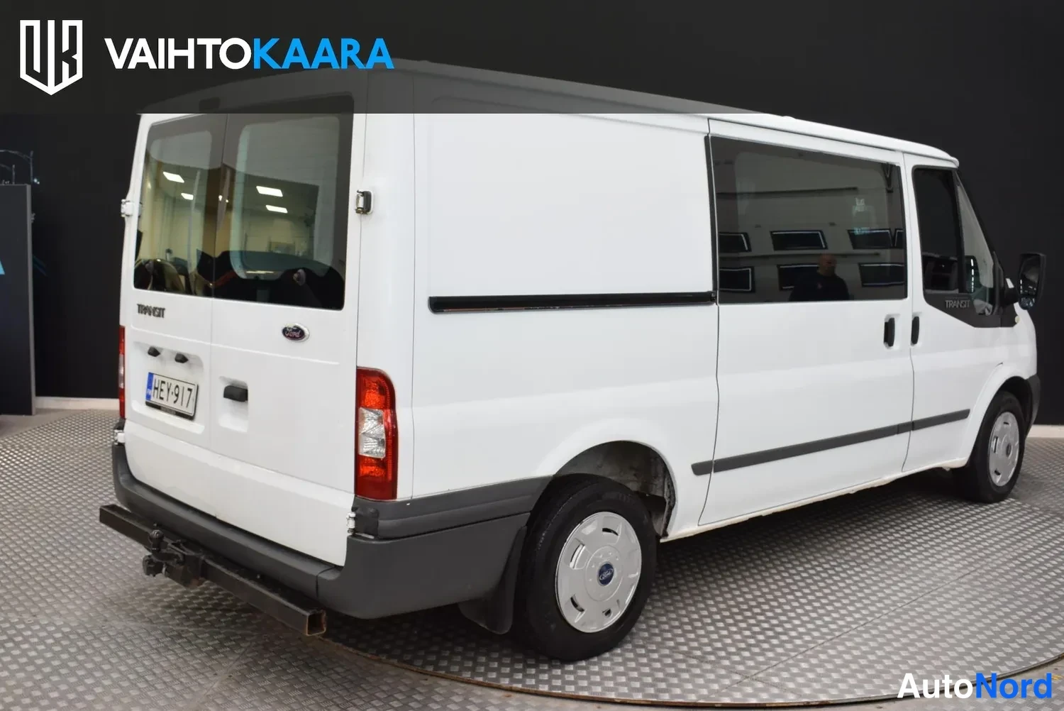 Takaviisto: Ford Transit -pakettiauto valkoisena takakulmasta, rekisterikilpi ja vetokoukku takapuskurissa.