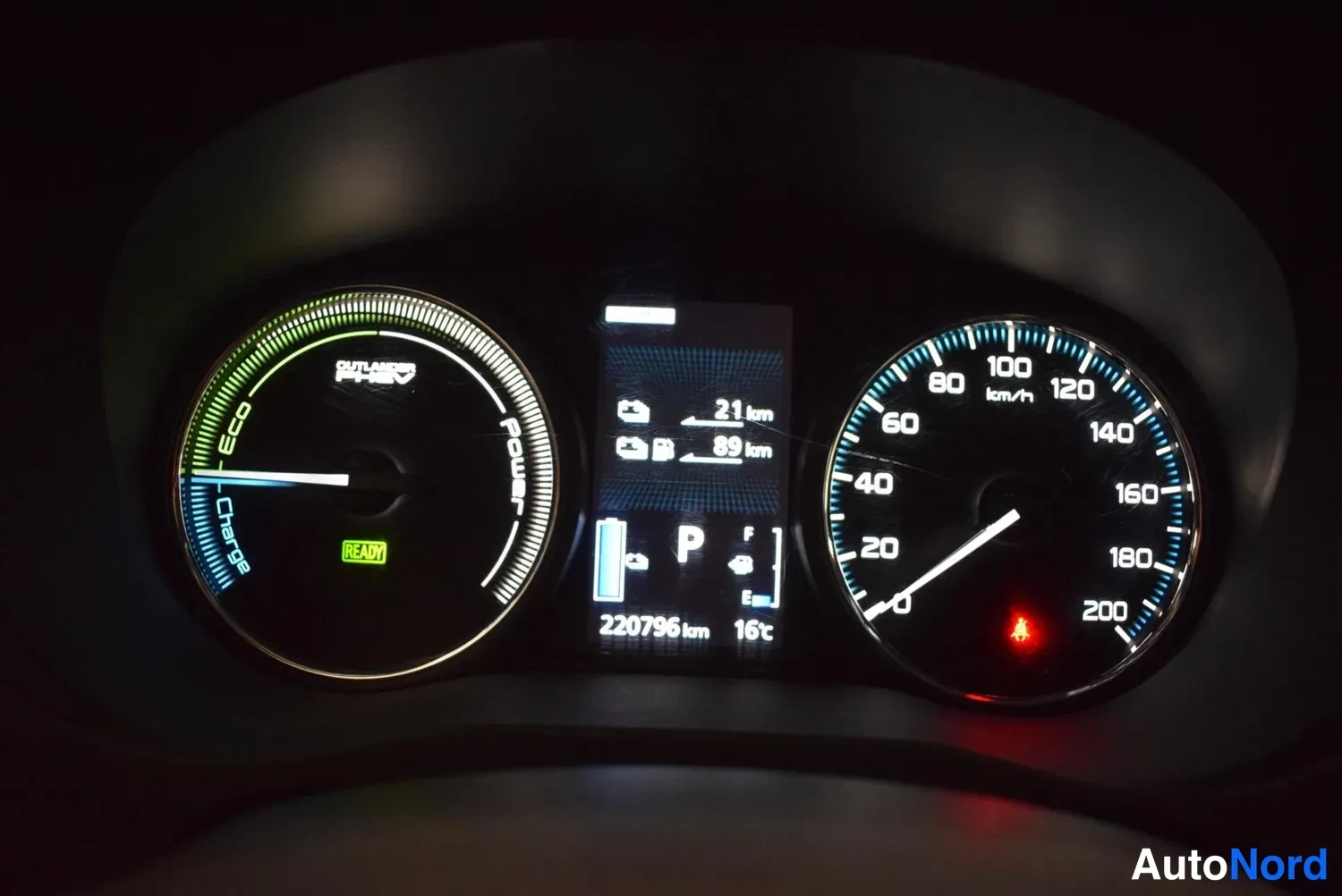Yksityiskohta: Mittaristo: vasemmalla ECO/Charge/Power-mittari READY-merkillä, keskellä näyttö jossa P, 21 km ja 89 km arvot, odometer 220796 km ja 16 °C, oikealla nopeusmitta