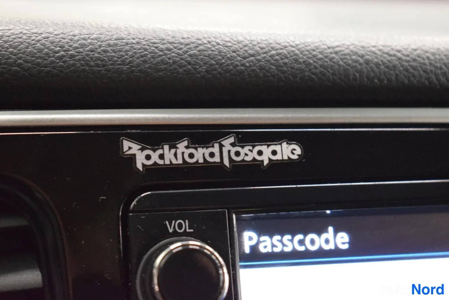 Muu: Lähikuva mustasta kojelautapaneelista, jossa on hopeinen 'Rockford Fosgate' -teksti, VOL-painike ja näytöllä sana 'Passcode'.